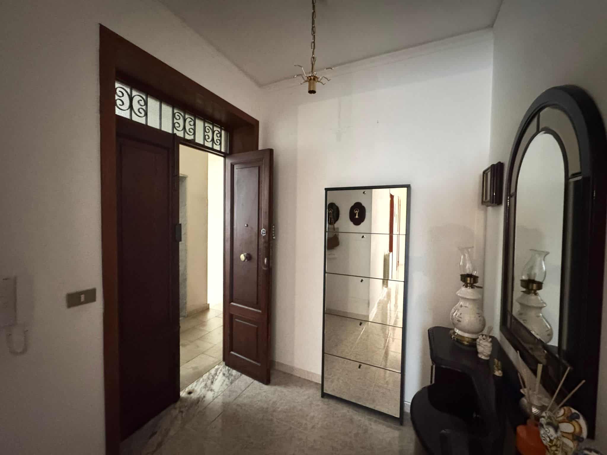Porta d'ingresso in legno con vetri decorativi e apertura verso l'interno, in un ingresso di casa elegante e accogliente.
