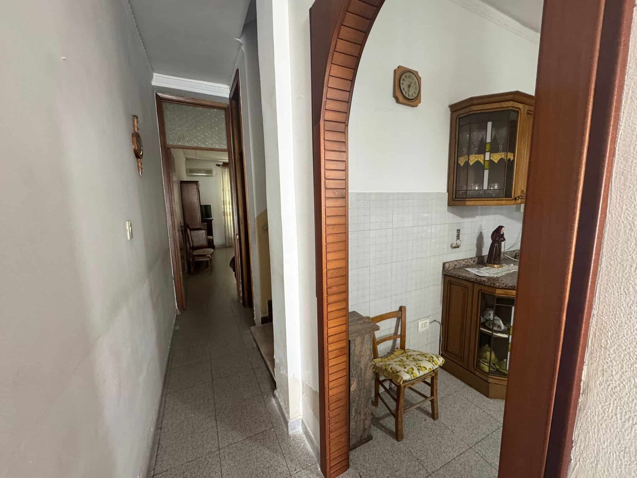 Interno di un appartamento con corridoio e ingresso, pareti bianche e pavimento in piastrelle, arredamento classico e dettagli in legno.