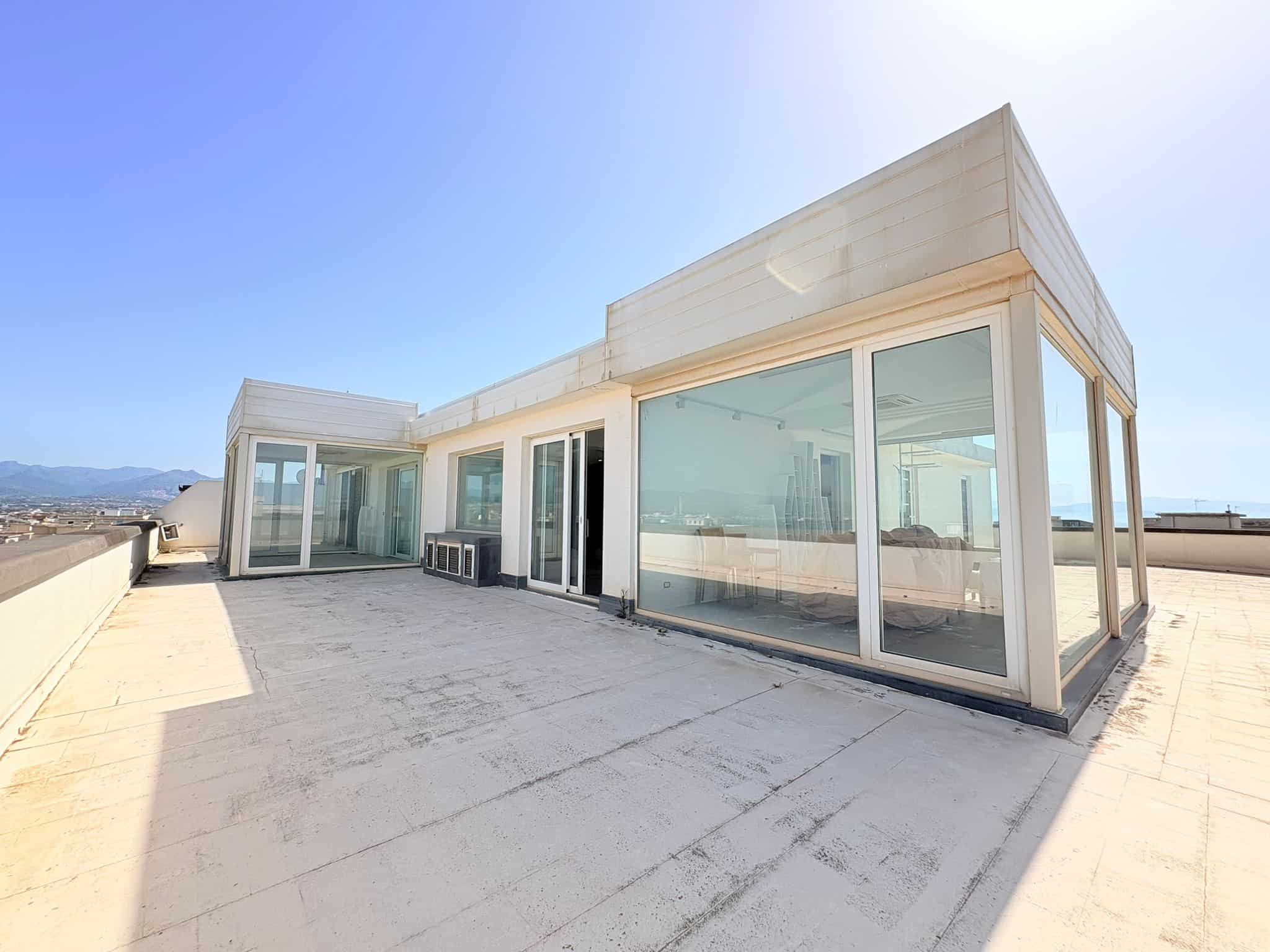 Balcone panoramico di un edificio moderno con ampie vetrate e vista sulla città e le montagne circostanti, ideale per relax e intrattenimento all'aperto.