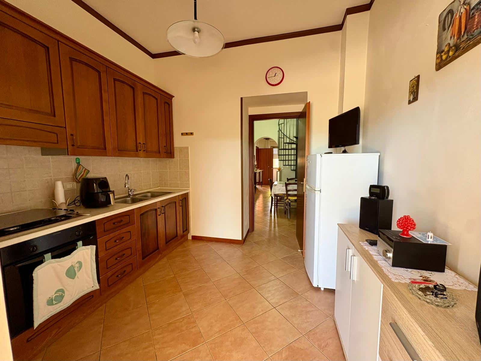 Cucina abitabile con mobili in legno, frigorifero, forno e zona pranzo, in un appartamento di NextCasa, con accesso a un soggiorno e scale che portano al piano superiore.