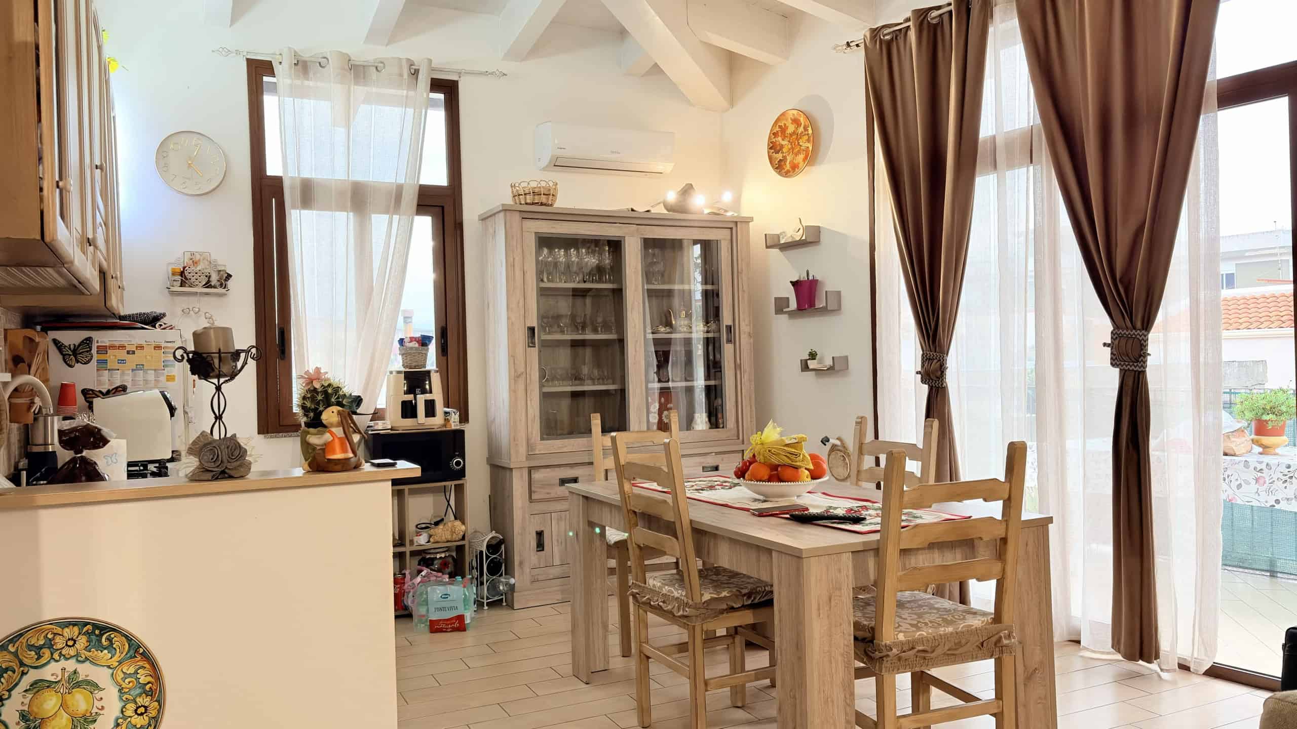 Porte scorrevoli in vetro che illuminano una zona pranzo luminosa e accogliente con tende marroni e arredi in stile rustico, ideale per case moderne e confortevoli.