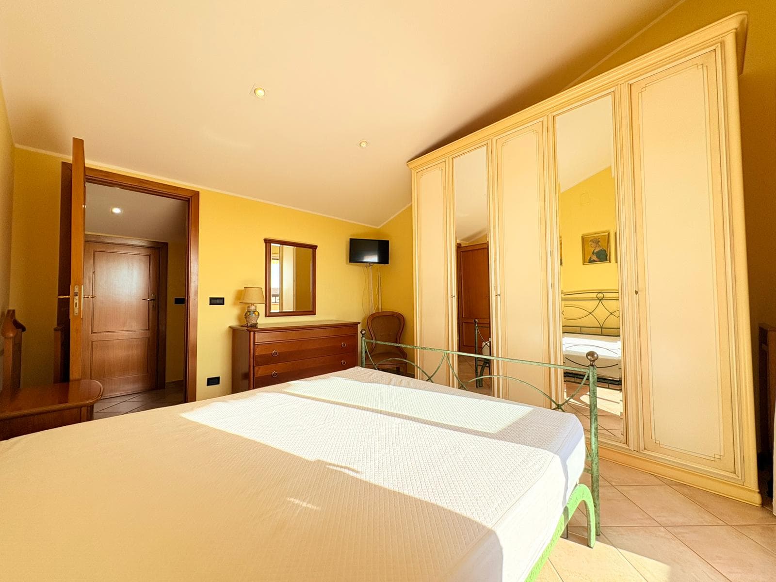Camera da letto luminosa con armadio a muro, mobili in legno e pareti gialle, ambiente accogliente e ben arredato.