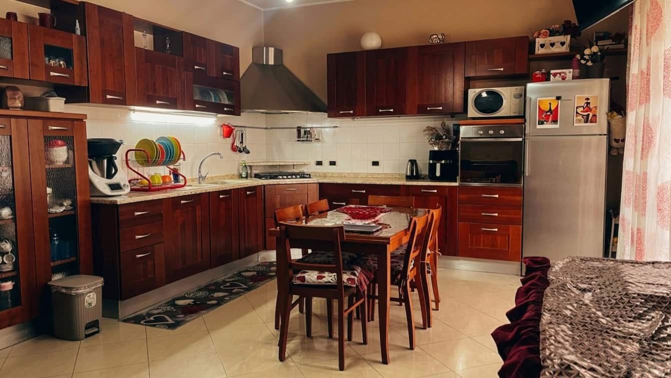 Cucina moderna con mobili in legno scuro, tavolo centrale e elettrodomestici integrati, ambiente accogliente e funzionale per la casa.