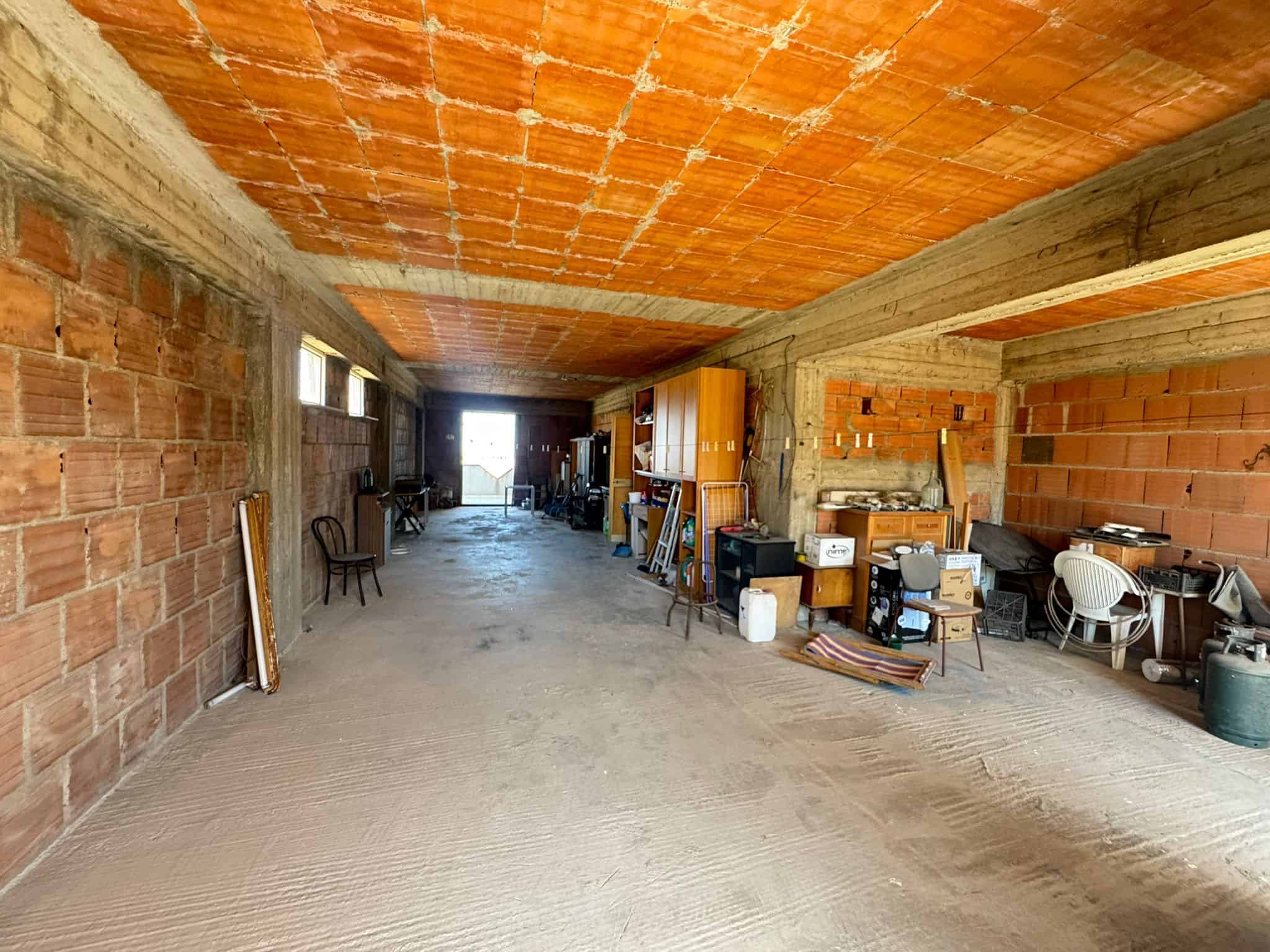 Interno di un garage o magazzino in costruzione con pareti in mattoni e soffitto in laterizio, spazio ampio e luminoso, pronto per finiture e personalizzazioni.
