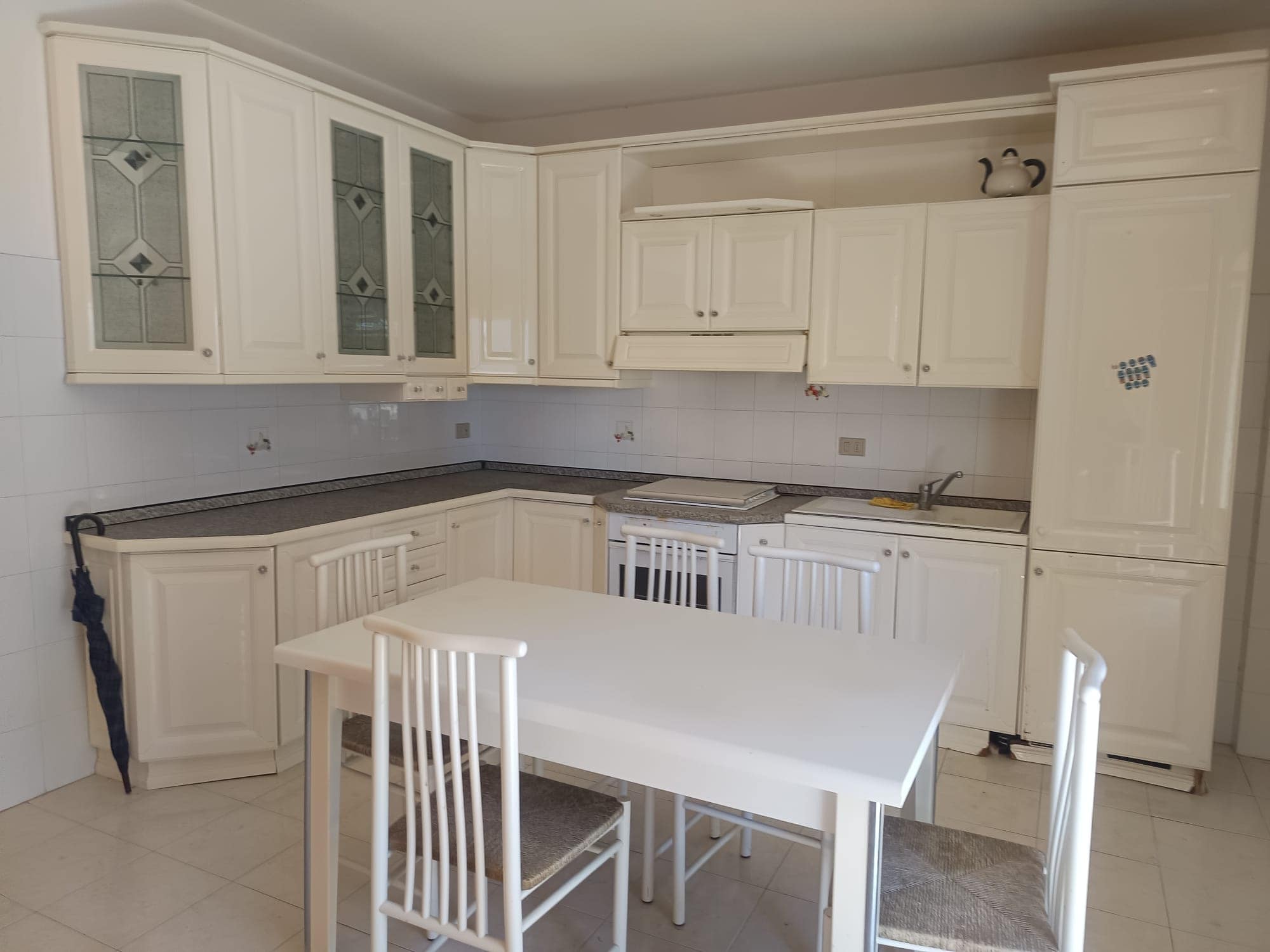 Pannello cucina bianco con mobili in stile classico, piano di lavoro in granito e zona pranzo con tavolo e sedie in soggiorno luminoso.