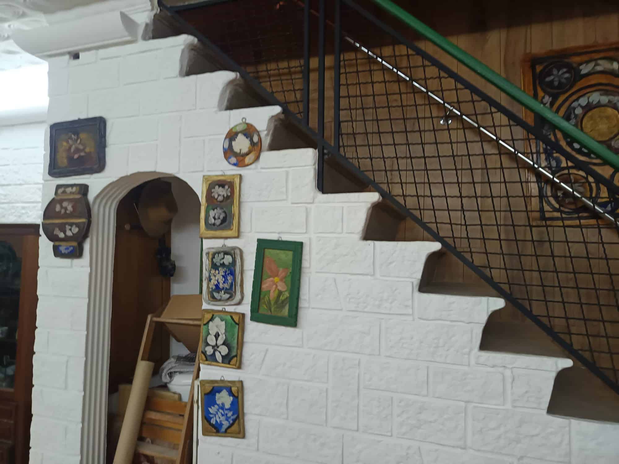 Scalinata interna con parete in mattoni bianchi decorata con quadri colorati e oggetti d'arte, ambiente accogliente e rustico.