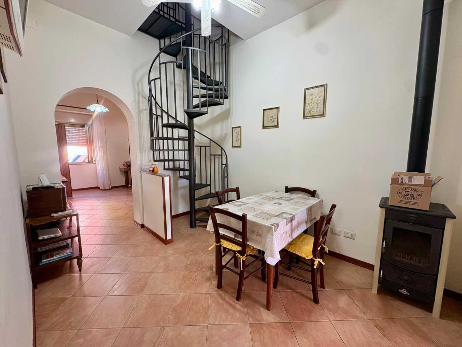 Soggiorno con tavolo da pranzo, scala a chiocciola e camino in stile rustico, ambiente accogliente e luminoso, arredamento funzionale e decorazioni eleganti, ideale per famiglie e ospiti.