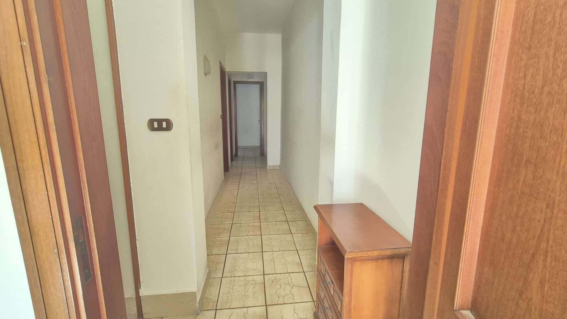 Spazio di corridoio luminoso e ben arredato in un appartamento, con pareti bianche, pavimento in piastrelle e mobili in legno, ideale per ambienti residenziali moderni.