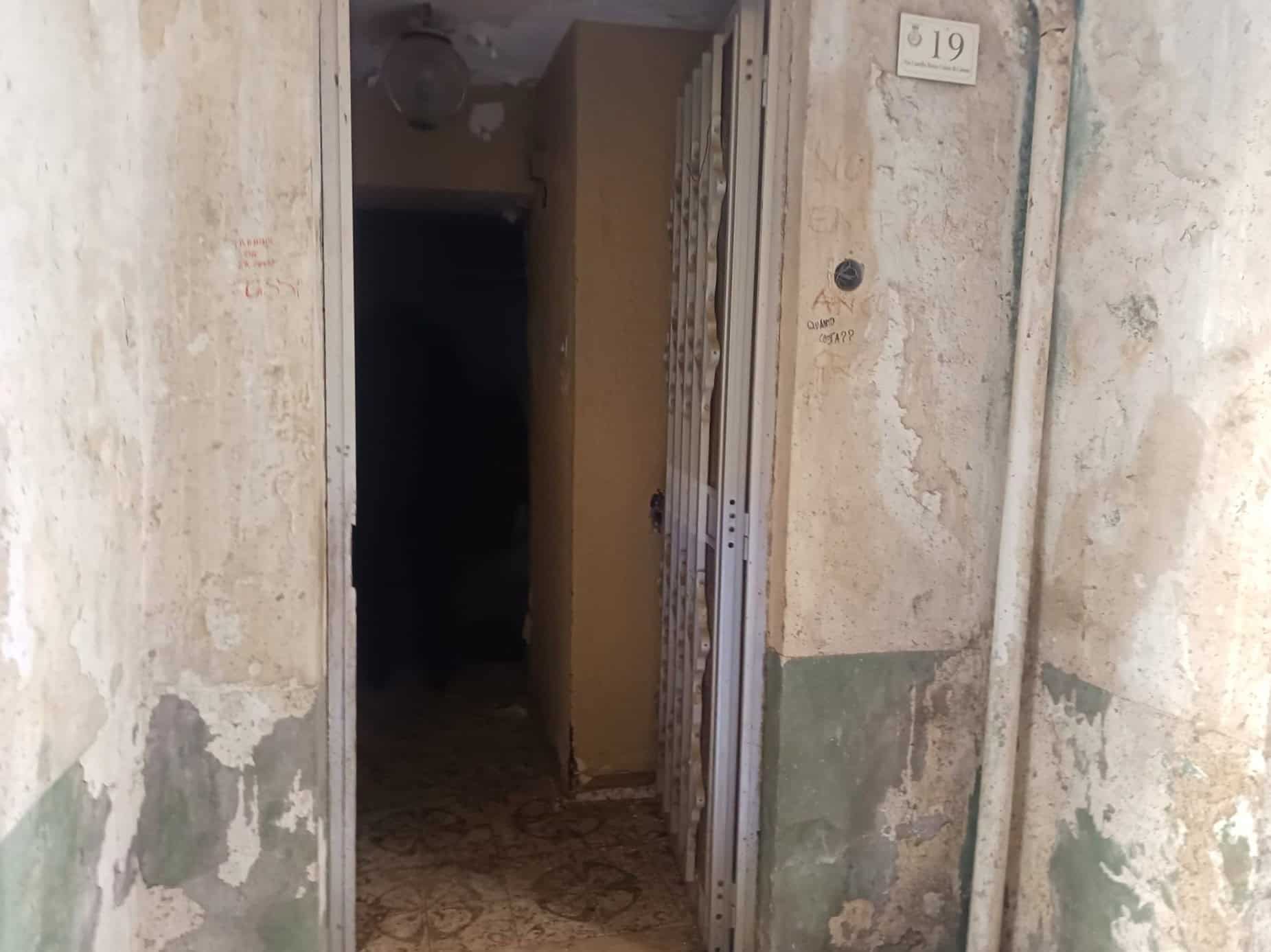 Una porta di ingresso in un edificio antico con pareti usurate e segni di deterioramento, in un ambiente che mostra segni di abbandono e mancanza di manutenzione.