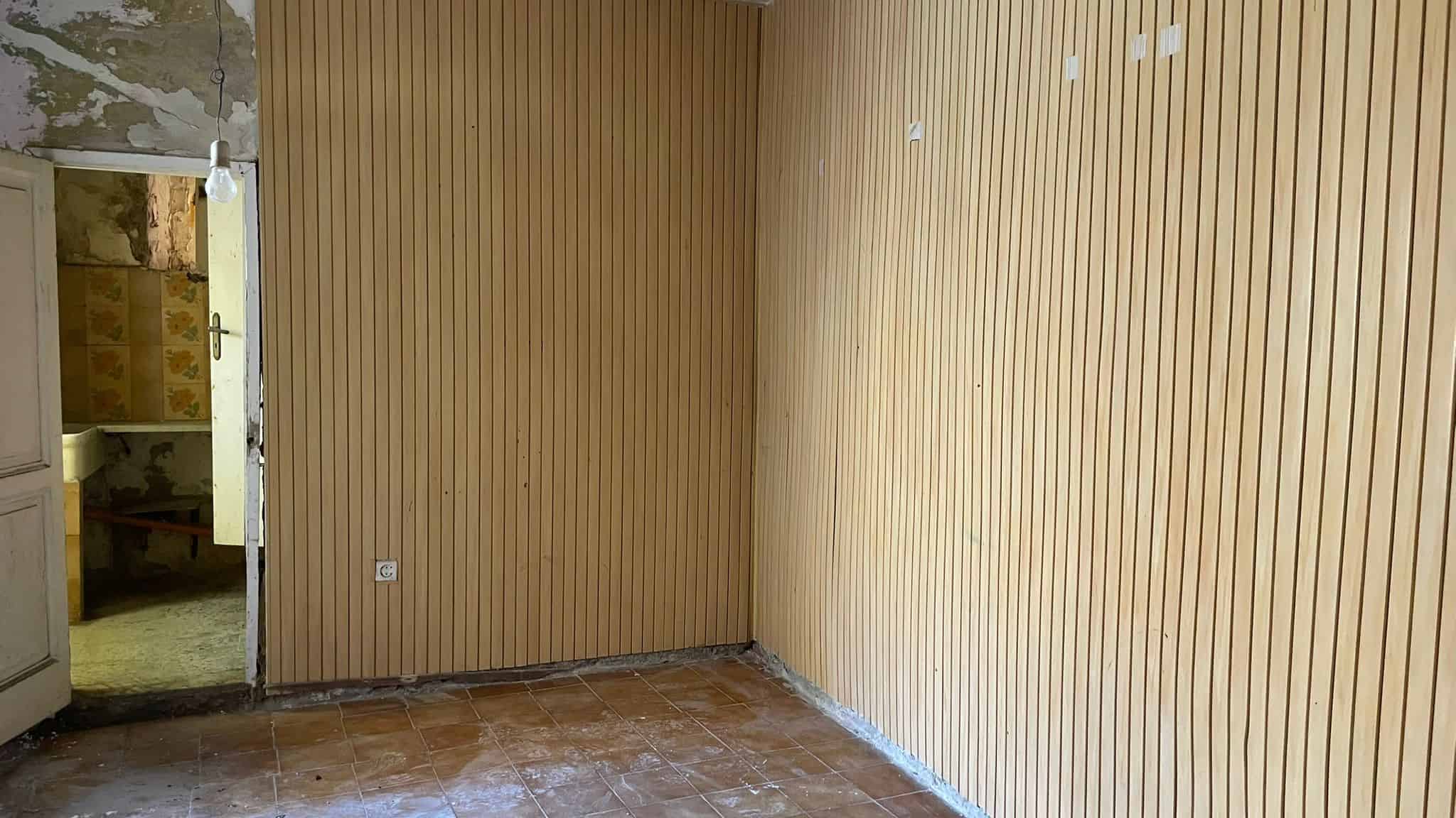 Ampia stanza con pareti in legno e pavimento in piastrelle, pronta per ristrutturazione, ideale per progetti di rinnovamento e interior design.