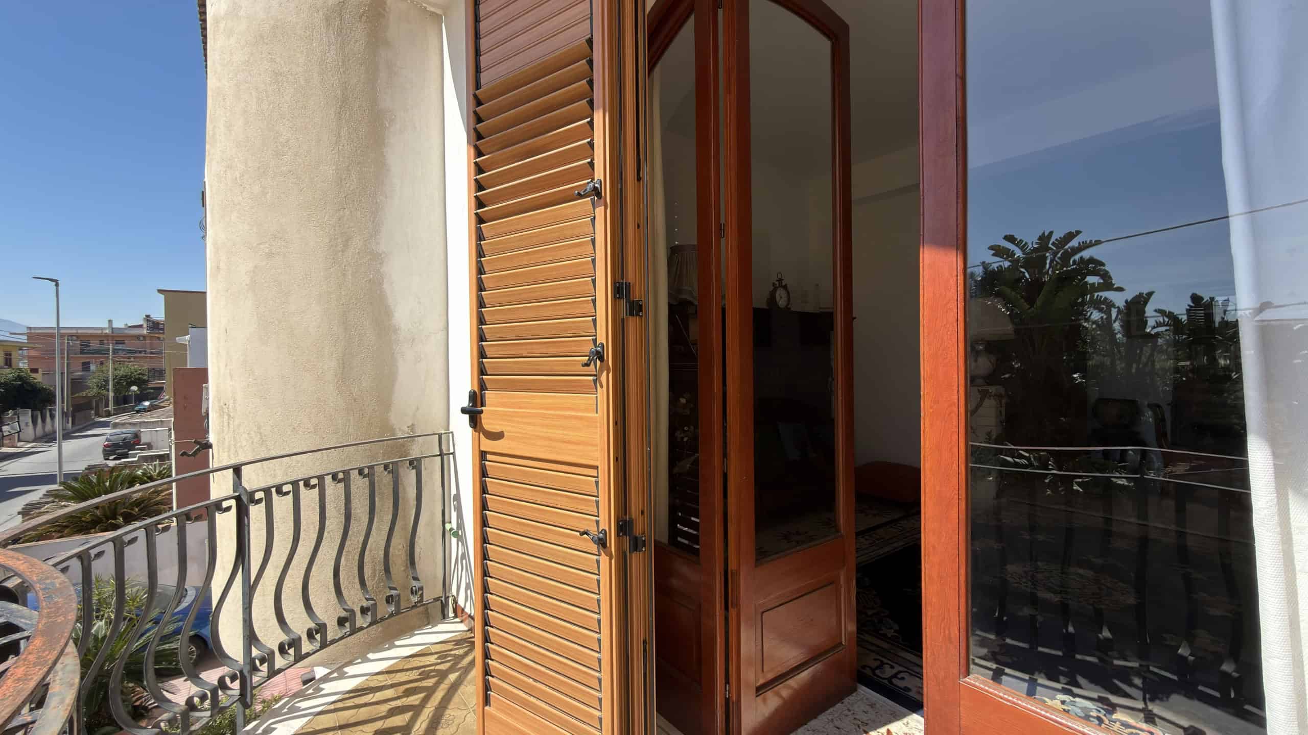Aggiungi una vista di una porta finestra in legno con persiane, che si apre su un balcone con ringhiera in ferro battuto, in un appartamento moderno a NextCasa, ideale per chi cerca soluzioni abitativ.