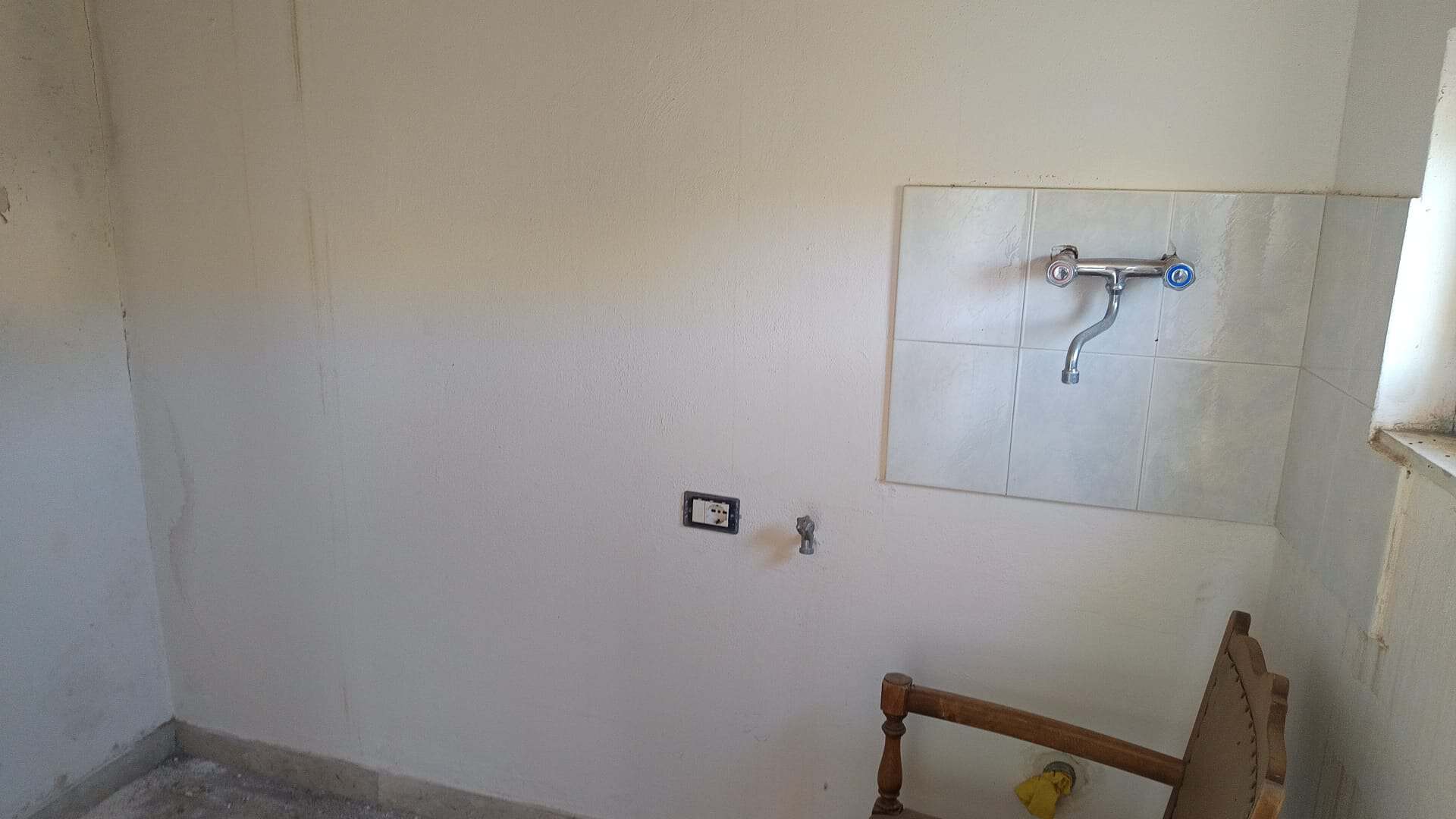 Lavanderia in fase di ristrutturazione con pareti bianche e pavimento in cemento, pronto per l'installazione di elettrodomestici e arredi. Spazio luminoso e funzionale, ideale per la preparazione e il.