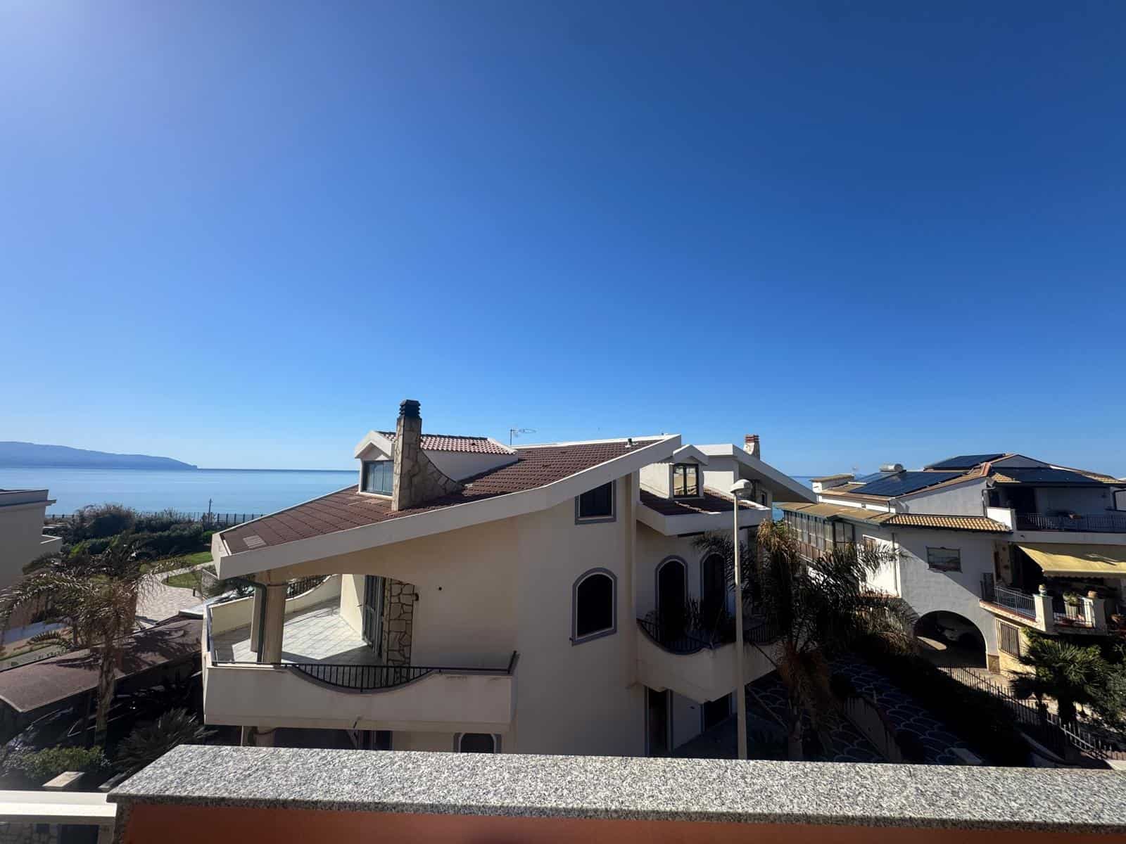 Ampia vista di una casa moderna con balconi e terrazze, situata vicino al mare sotto un cielo sereno, ideale per chi cerca una residenza con vista panoramica e accesso diretto alla spiaggia.