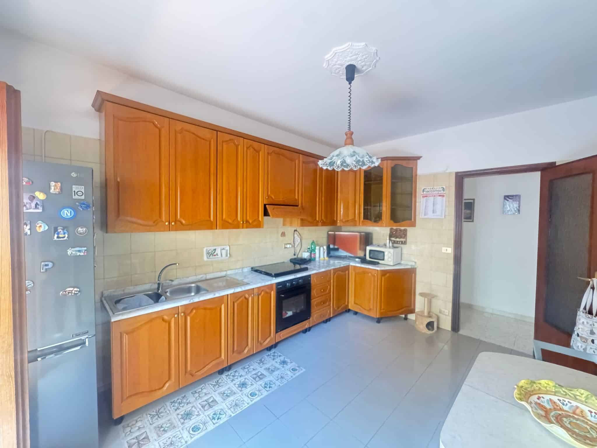 Piano cucina in stile classico con ante in legno, elettrodomestici moderni, e illuminazione centrale, ambiente luminoso e funzionale ideale per la preparazione dei pasti.
