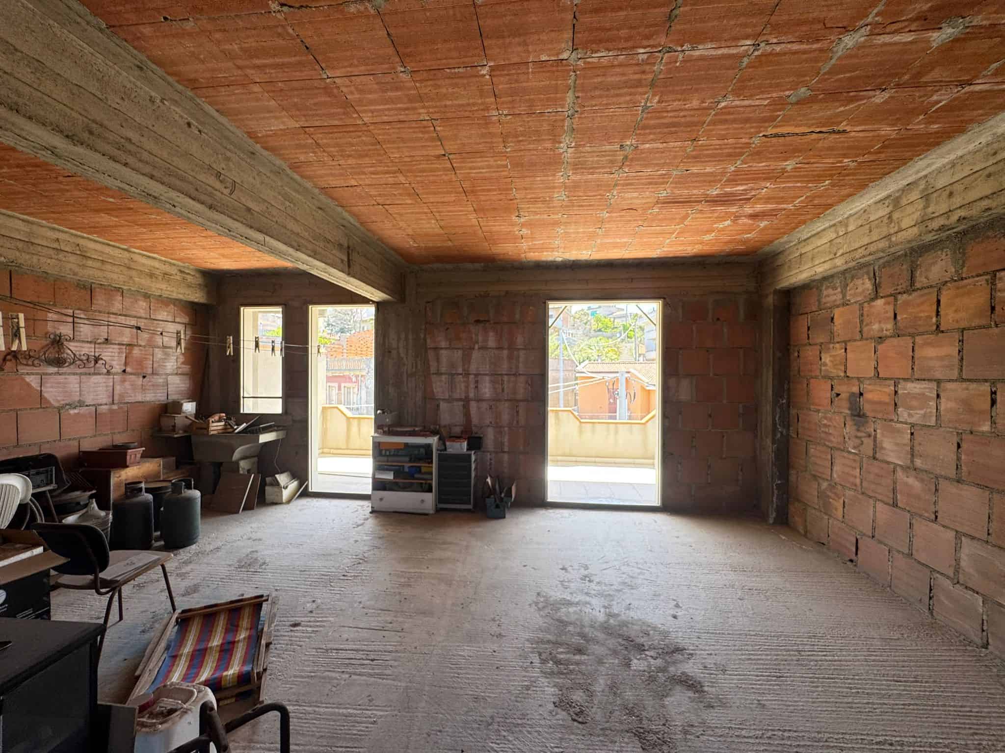 Ampia stanza in costruzione con pareti in mattoni rossi e soffitto in cemento, pronta per essere rifinita e personalizzata, ideale per residenze o uffici moderni.