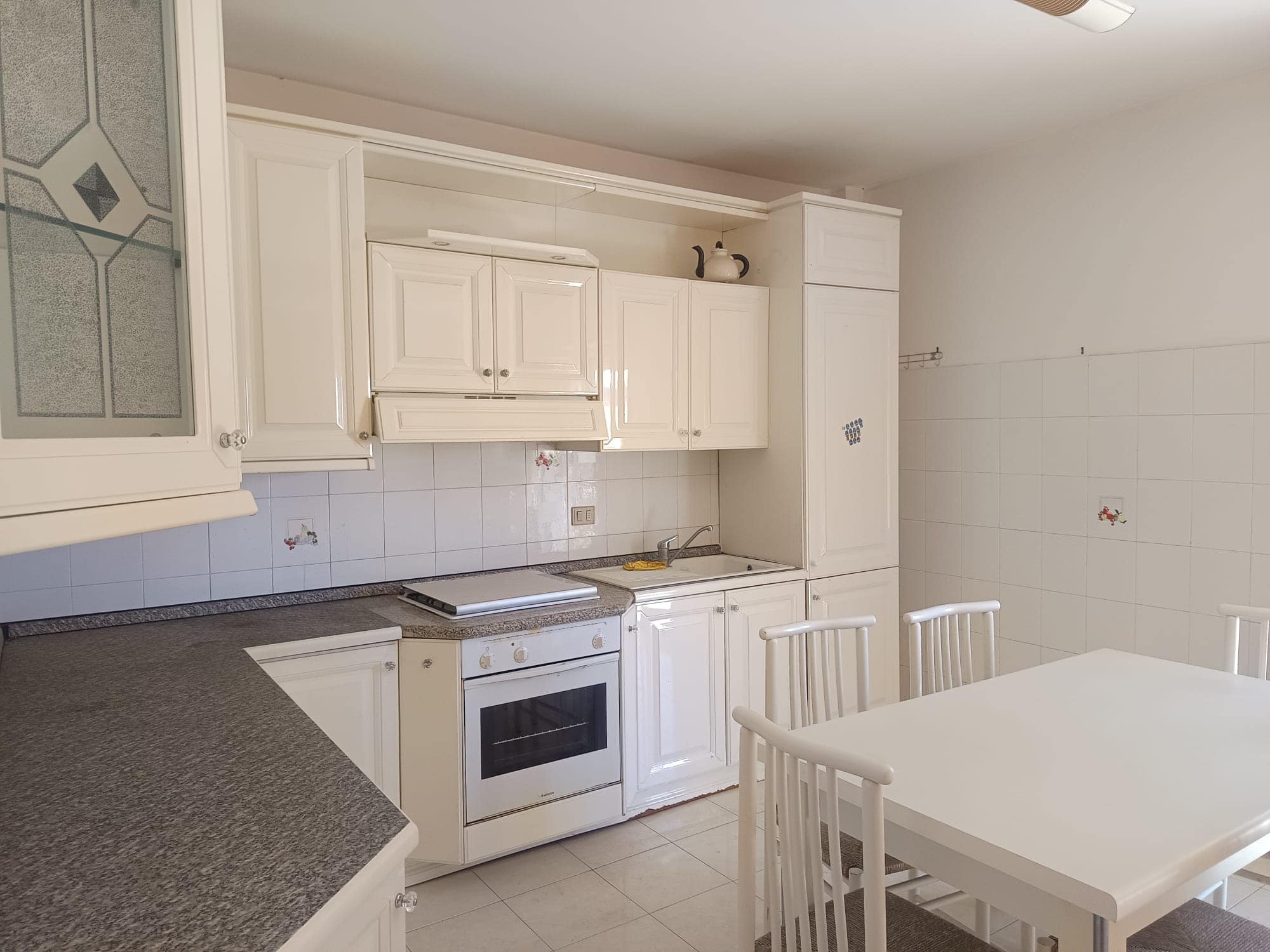 Pannello di cucina bianco con elettrodomestici e tavolo da pranzo in una cucina moderna e luminosa. Ideale per ambienti residenziali, con spazio funzionale e stile minimalista.