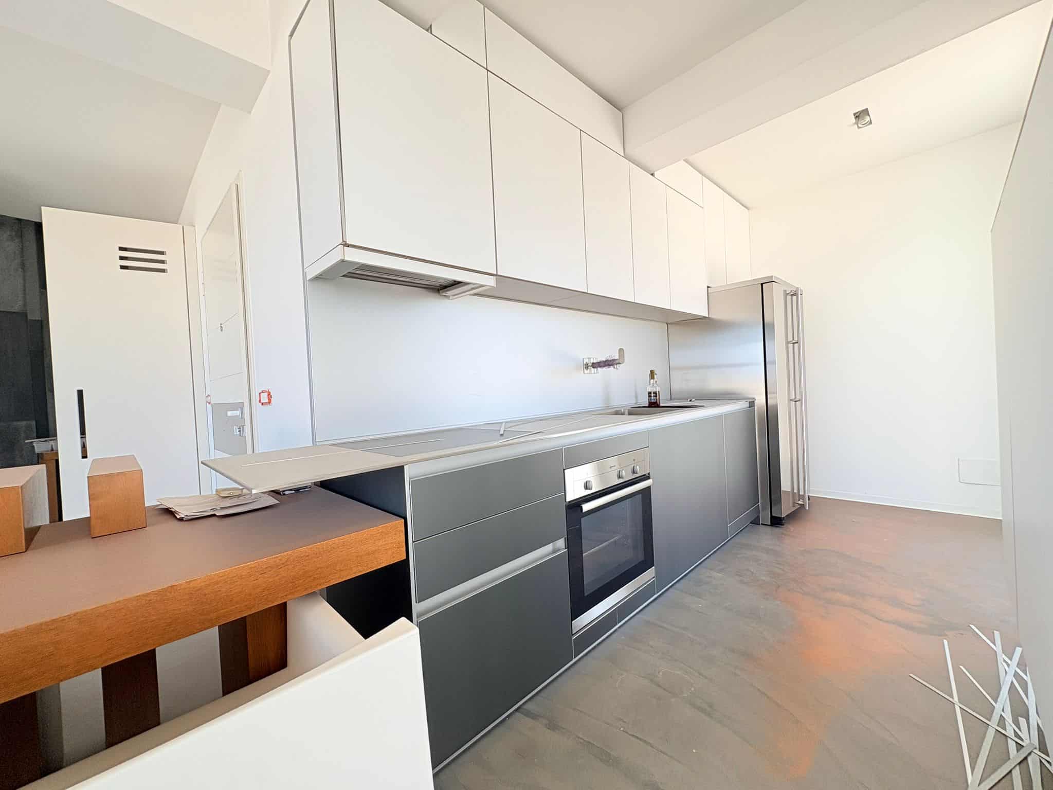 Un'ampia cucina moderna con mobili bianchi e grigi, elettrodomestici integrati e spazio luminoso, ideale per vivere e cucinare in un ambiente funzionale e elegante.