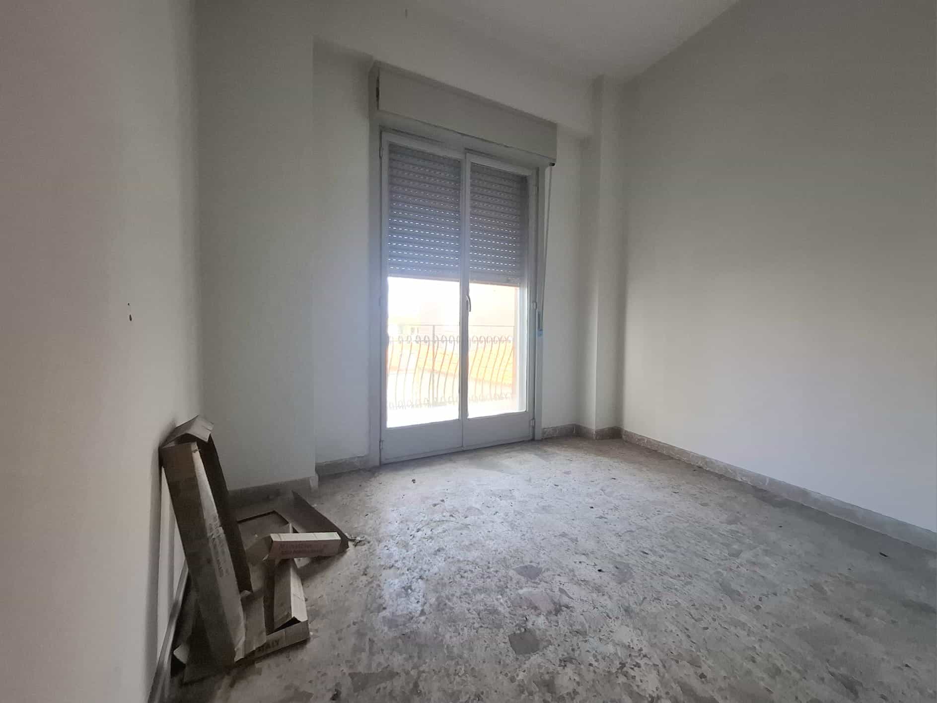 Porte finestra scorrevole con balcone in un appartamento vuoto, luce naturale che entra nella stanza.