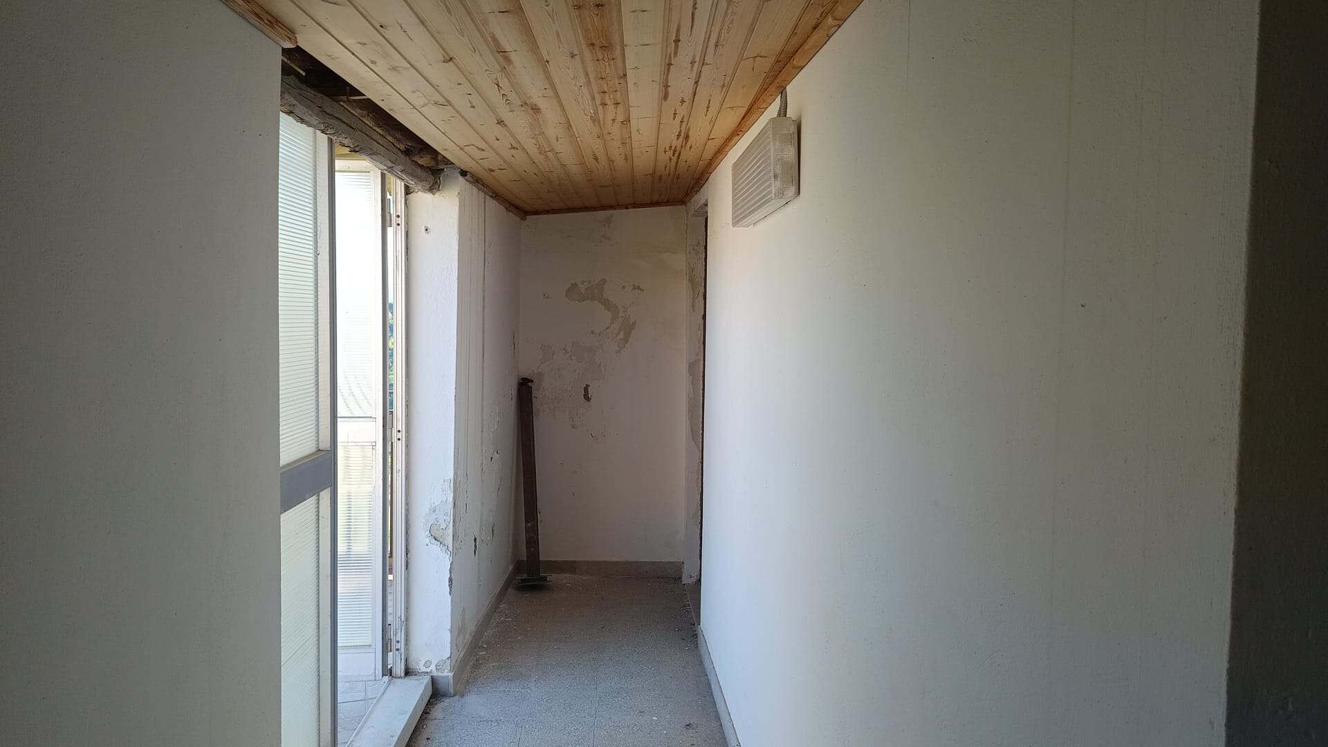 Aggiunta di un'immagine di un interno di un appartamento in fase di ristrutturazione, con pareti bianche e soffitto in legno, che mostra un balcone o una finestra grande.