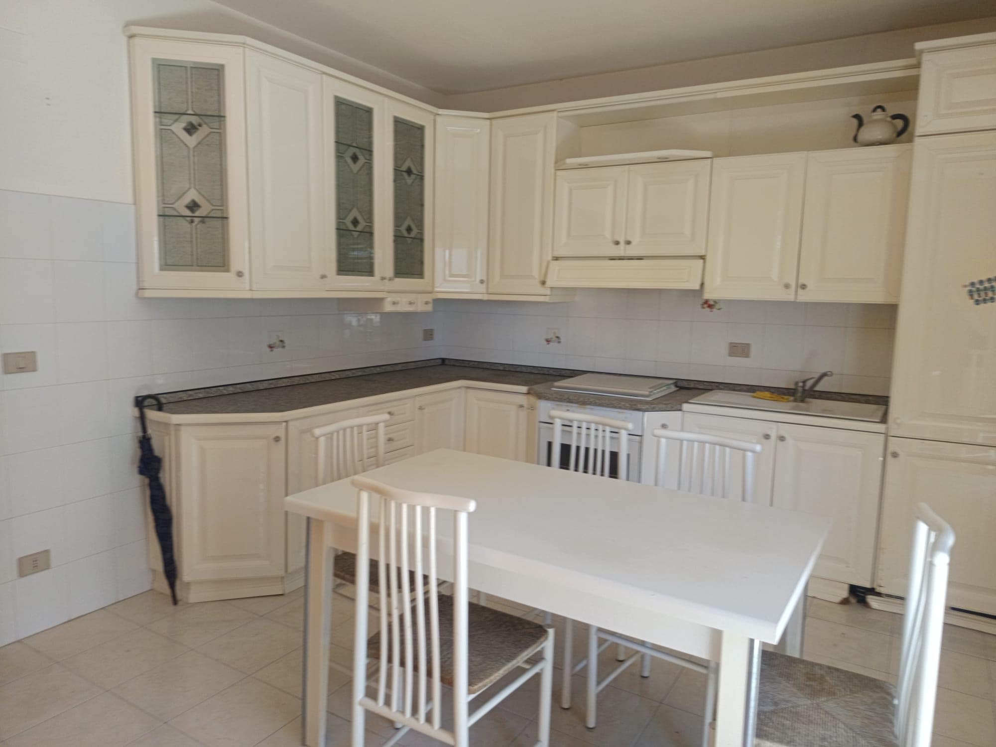 Cucina moderna con mobili bianchi, piano in granito e zona pranzo con tavolo e sedie in stile classico, ambiente luminoso e funzionale.