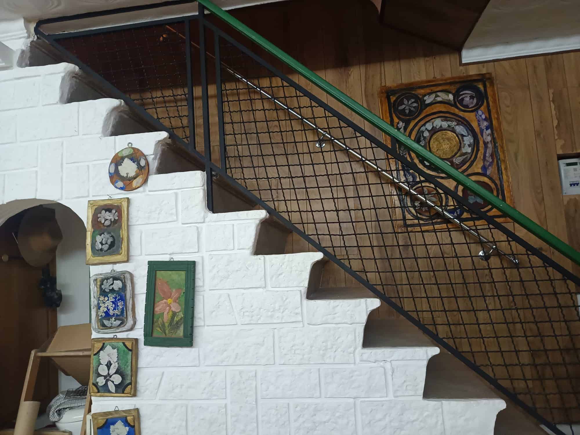 Escaliera interna con ringhiera in metallo nero e pannelli in legno, decorata con quadri e oggetti artistici, in un ambiente domestico accogliente e ben arredato.