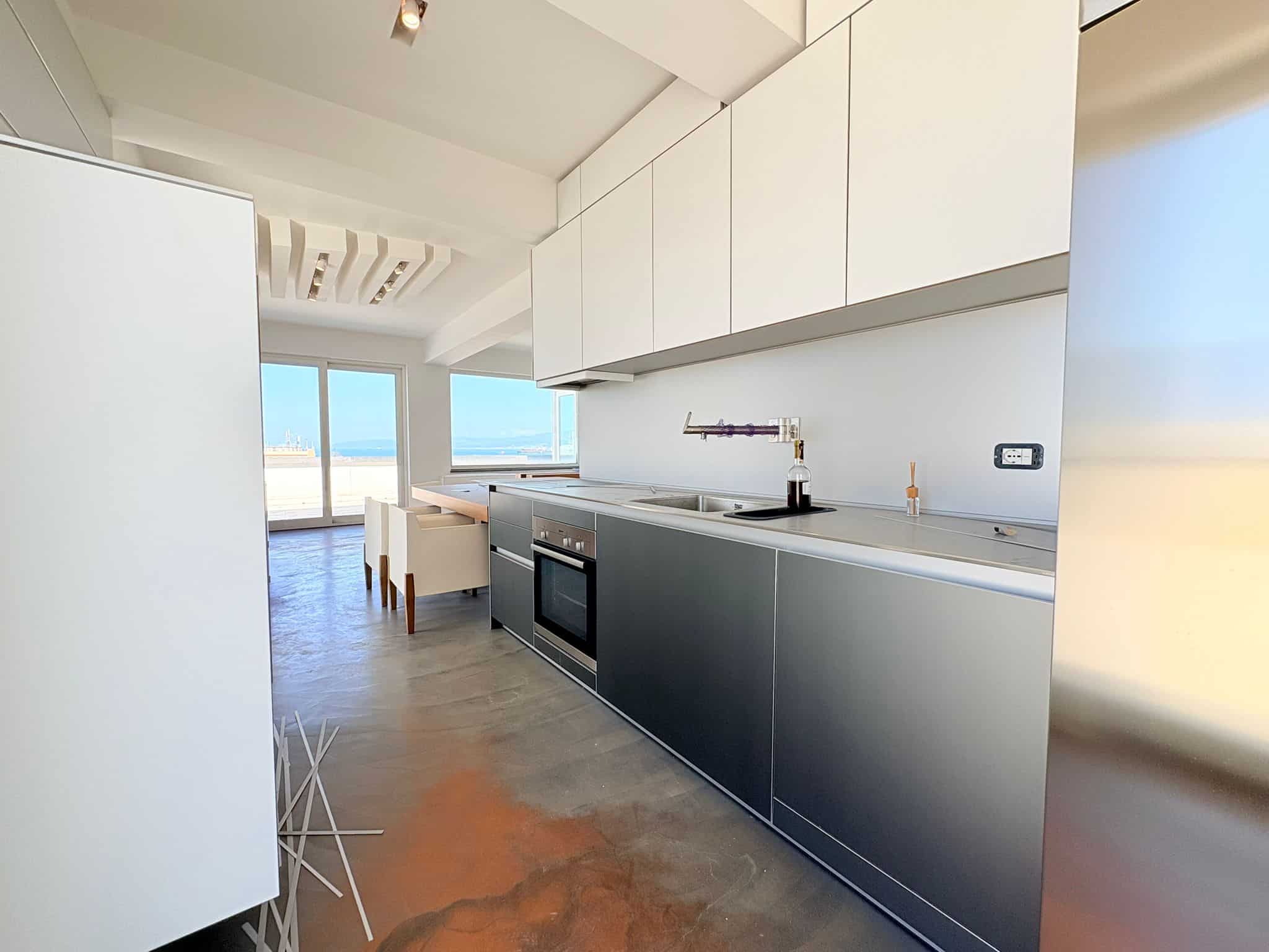 Pannello cucina moderna con vista sul mare, arredamento minimalista e superfici lucide, ambiente luminoso e spazioso ideale per vivere in relax e stile.