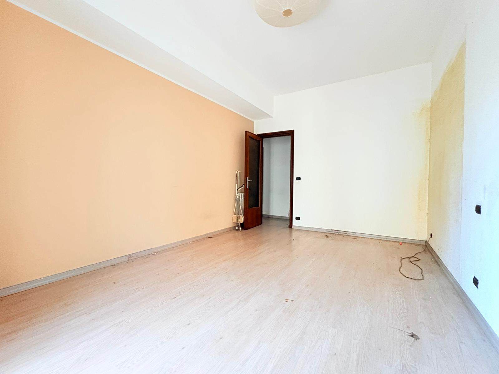 Stanza vuota in affitto o vendita con pareti colorate e pavimento in legno, pronta per arredare, in un appartamento di NextCasa, agenzia immobiliare italiana.