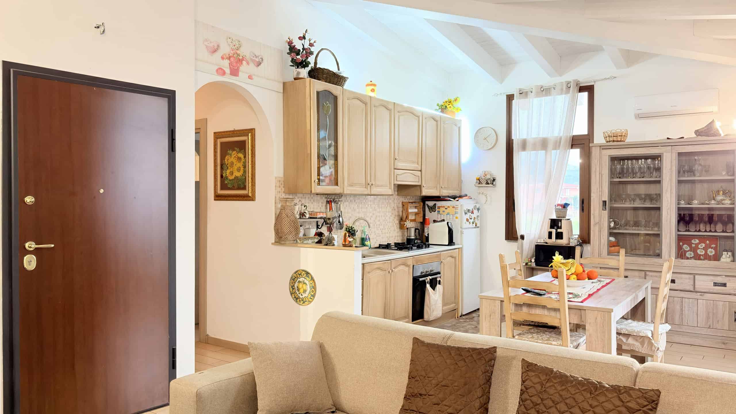 Cucina moderna in stile rustico con mobili in legno chiaro, tavolo da pranzo e accessori decorativi, ambiente luminoso e accogliente.