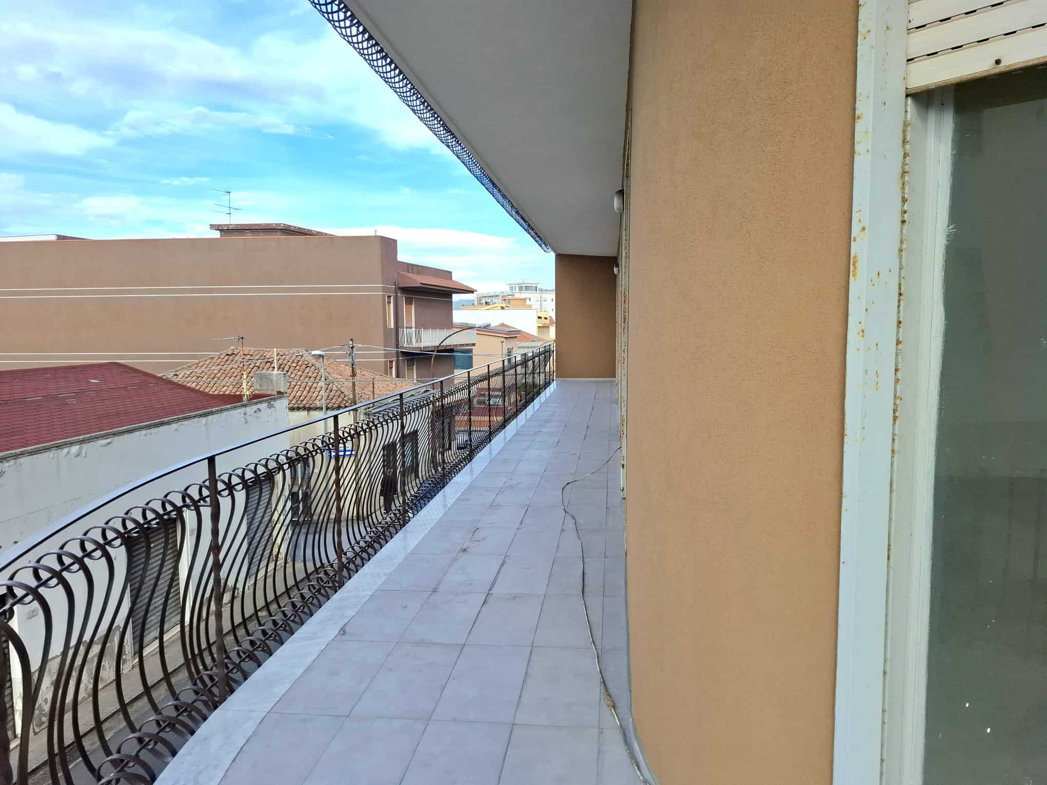 Balcone di un appartamento con ringhiera in ferro battuto e vista su tetti e cielo azzurro, in un contesto urbano.