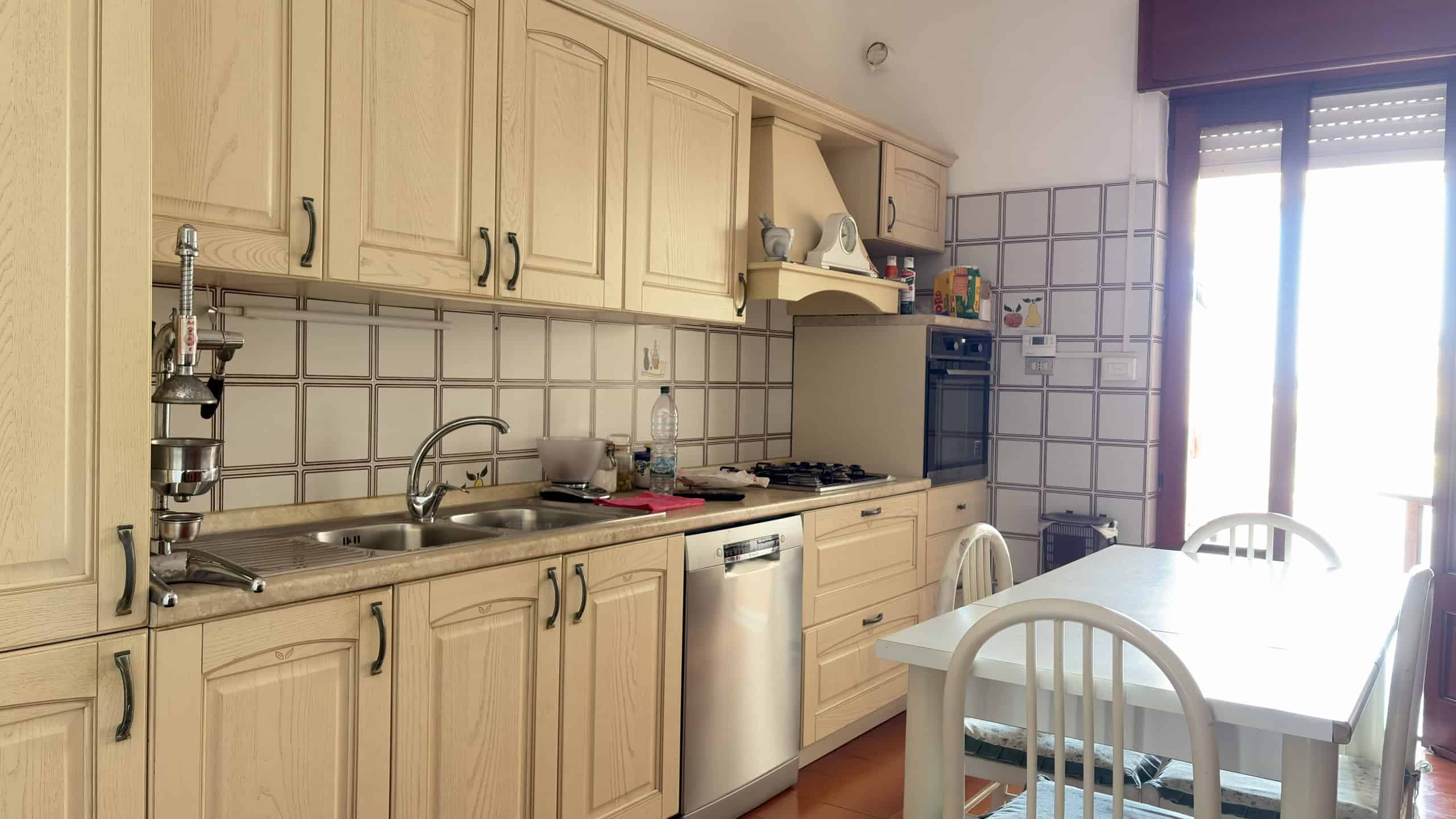 Pannello di cucina in legno chiaro con elettrodomestici moderni e spazio per la colazione, illuminata dalla luce naturale proveniente dalla finestra con persiana.