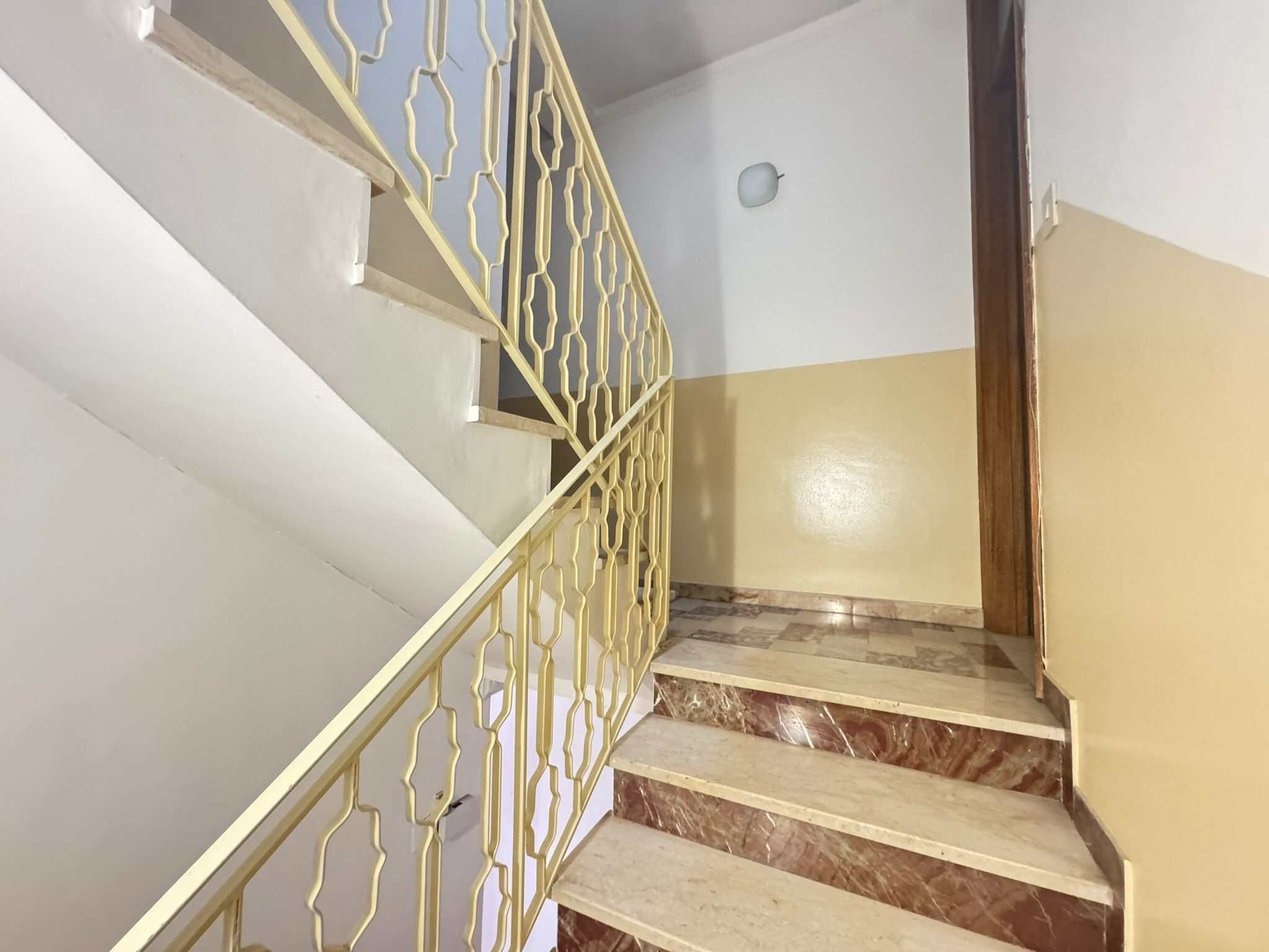 Scalinata interna con ringhiera dorata e pareti bianche e beige, ingresso di un edificio residenziale moderno.
