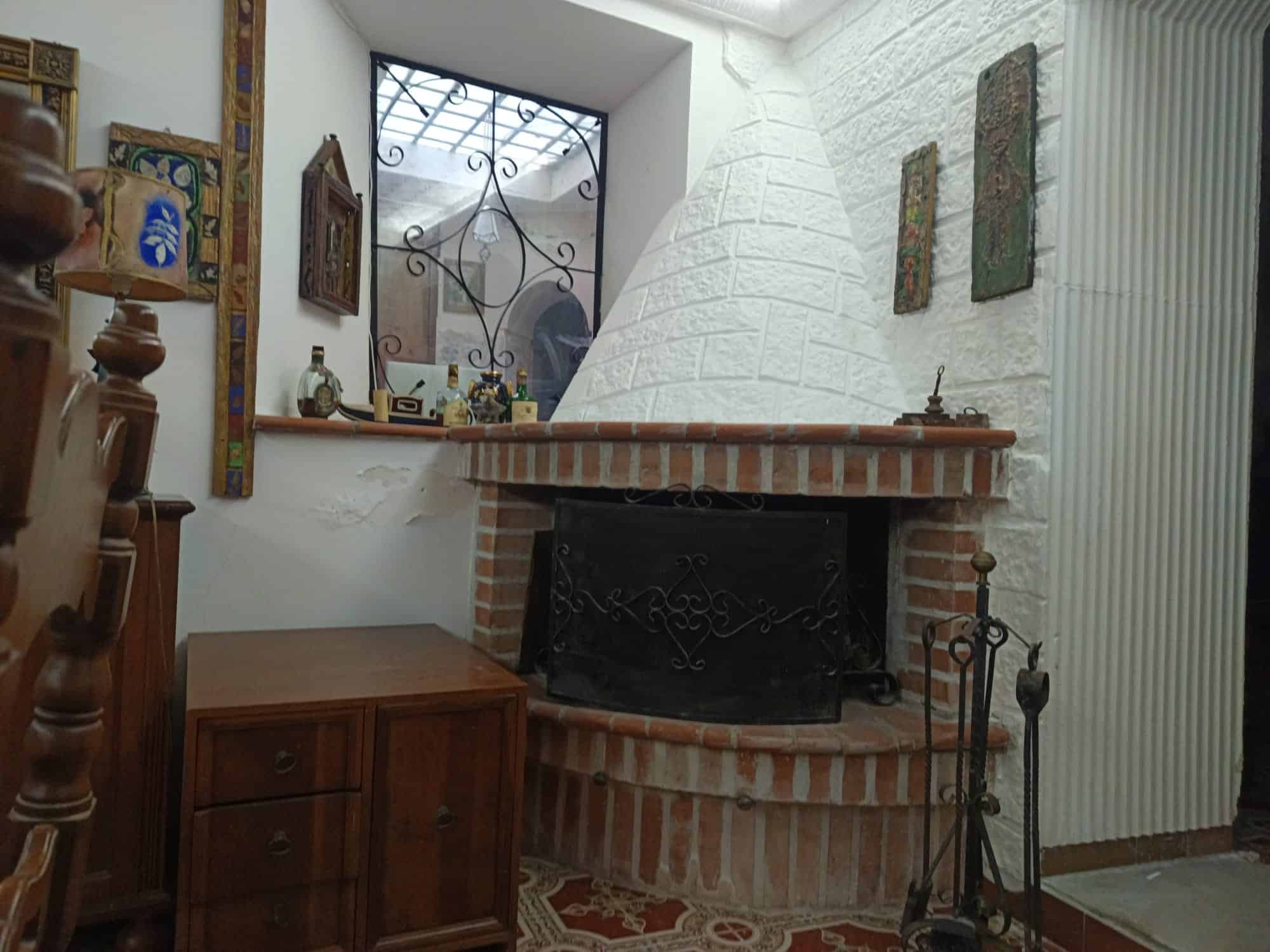 Il camino in stile rustico con struttura in mattoni e parete bianca, decorato con quadri e oggetti d'antiquariato, in un ambiente accogliente e tradizionale.