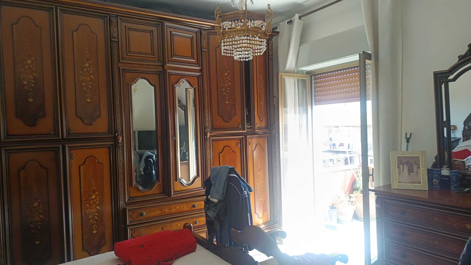 Armadio antico in legno massello con dettagli decorativi, posizionato in una camera da letto luminosa con finestra aperta e tende bianche.