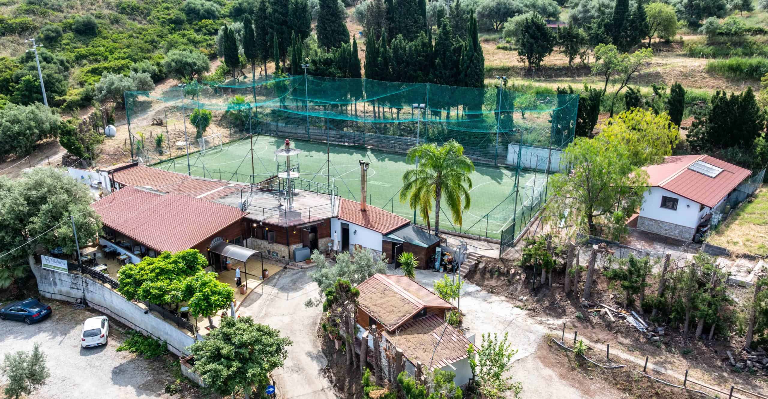 Ampio campo da tennis all'aperto circondato da natura e alberi, con strutture sportive e aree verdi, ideale per attività ricreative e sport all'aperto in un ambiente tranquillo e immerso nel verde.