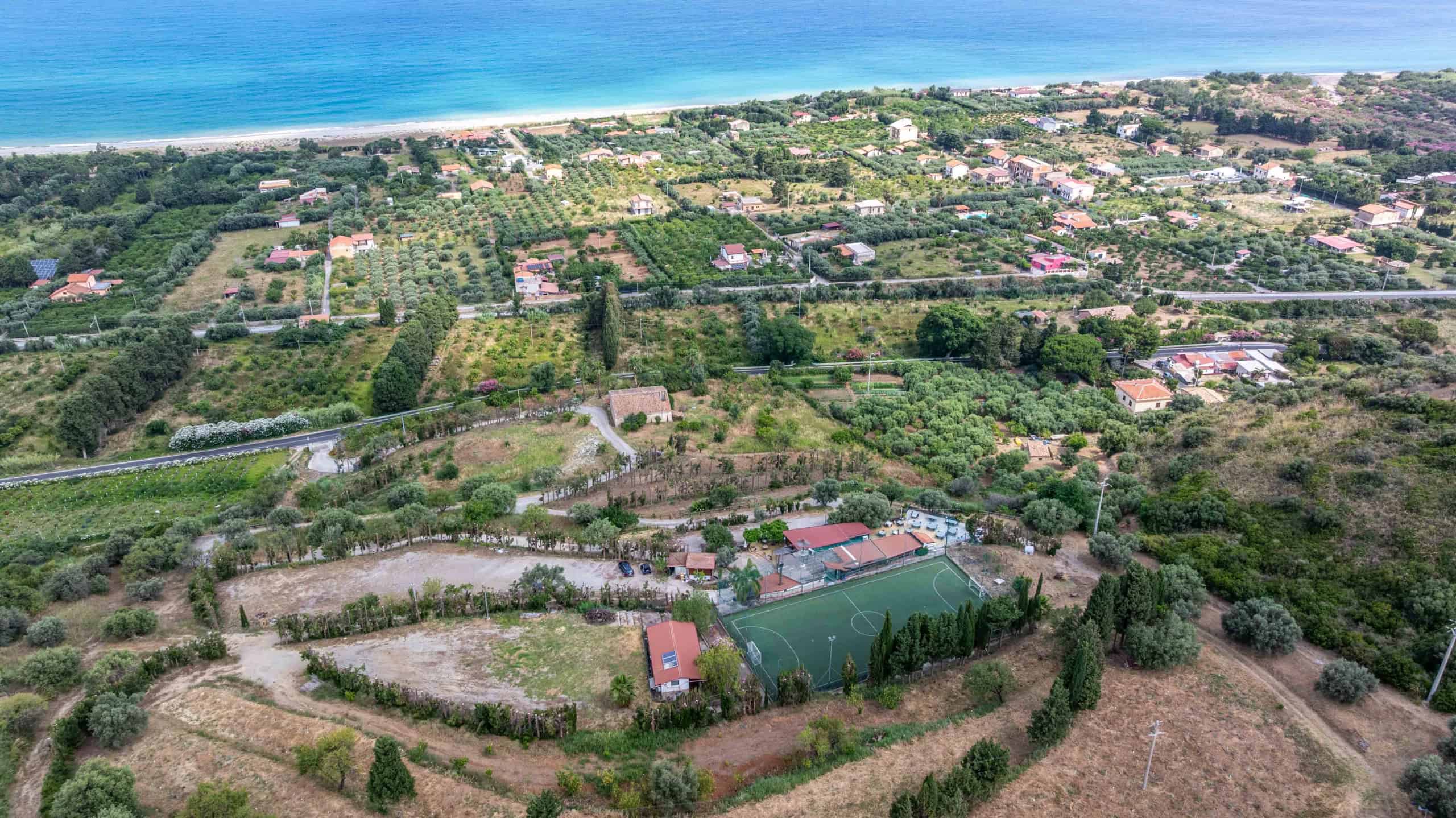Ampio panorama di campagna con vista mare, terreni coltivabili, strade rurali e alcune abitazioni, ideale per investimenti immobiliari e sviluppo di proprietà in zona tranquilla e naturale.