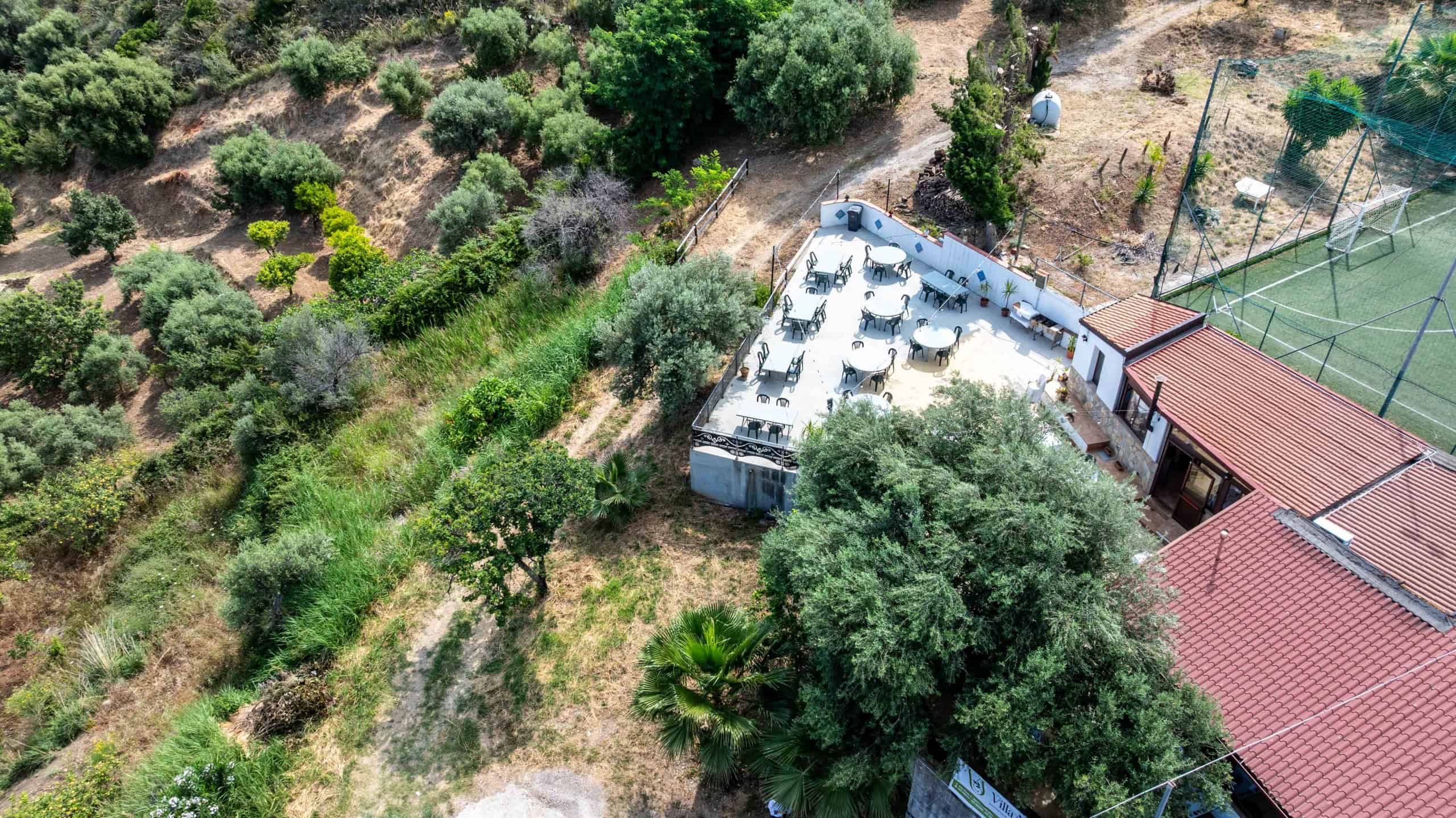 Ampio campo da tennis all'aperto con recinzione, situato vicino a un'area verde con alberi e piante, ideale per sport e attività ricreative all'aperto.