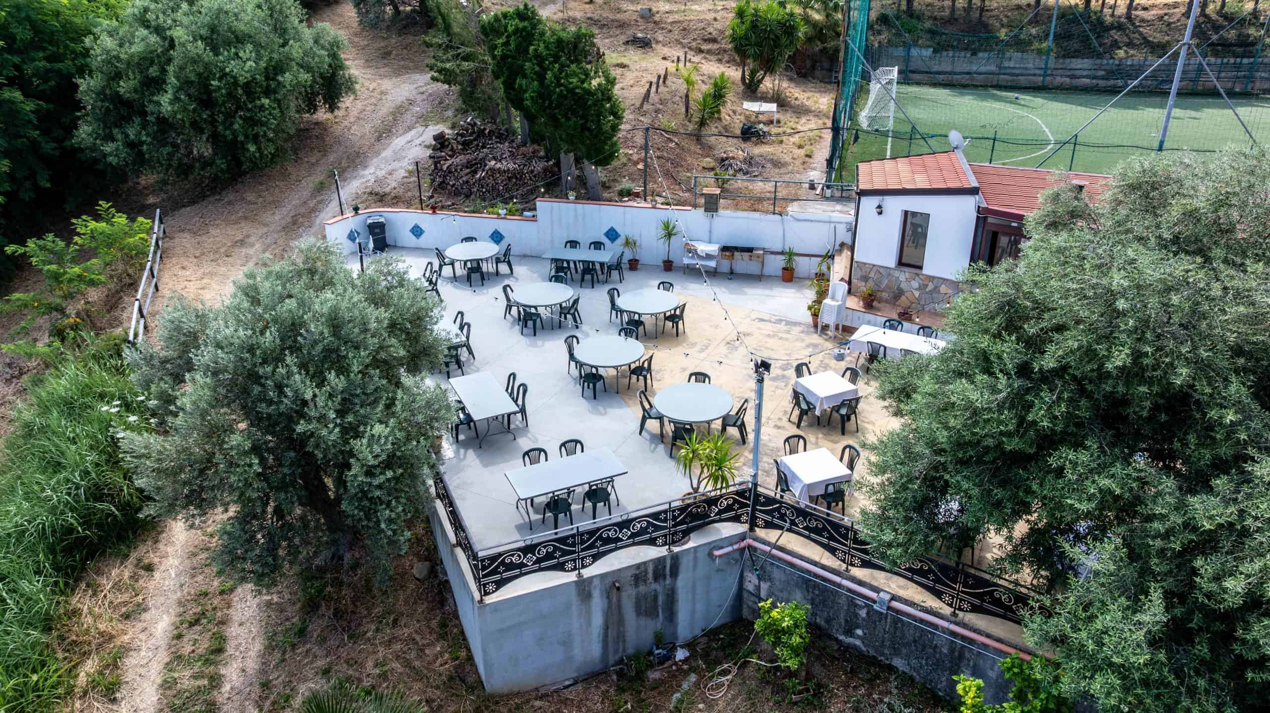Elegante area esterna con tavoli e sedie, circondata da vegetazione e alberi, ideale per relax e socializzazione all'aperto. Spazio ben curato con vista panoramica, perfetto per eventi o momenti di co.