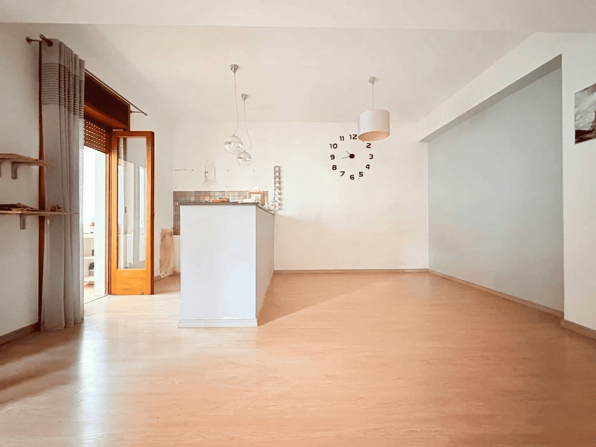 Il soggiorno luminoso e spazioso con pareti bianche, pavimento in legno chiaro e grandi finestre che lasciano entrare molta luce naturale, ideale per vivere e ricevere ospiti.