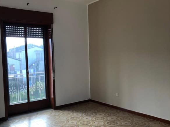 Aggiunta di un'immagine di una stanza vuota con porta finestra e vista esterna, con pavimento decorato e pareti neutre, ideale per annunci immobiliari o ristrutturazioni.