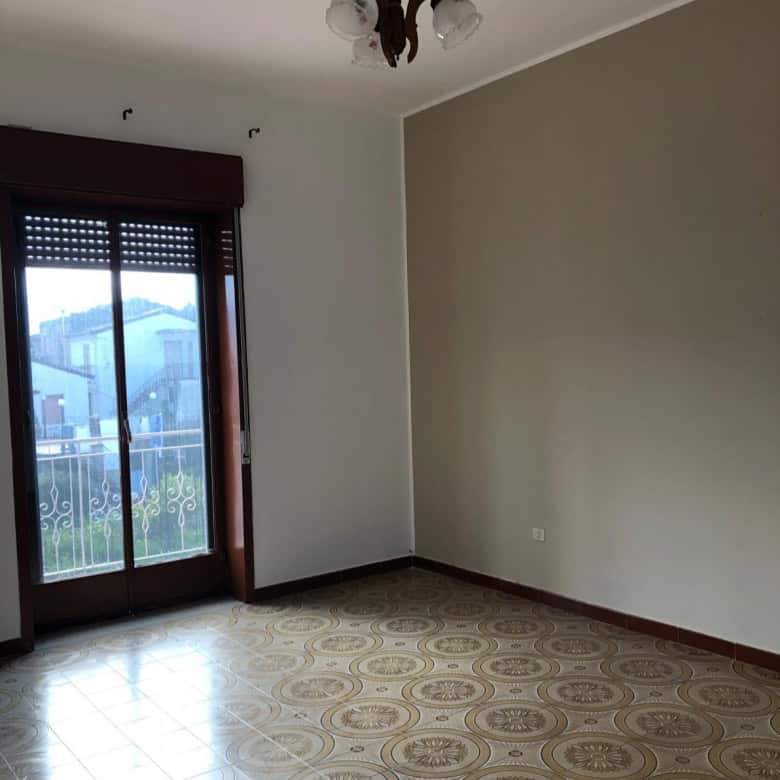Aggiunta di un'immagine di una stanza vuota con porta finestra e vista esterna, con pavimento decorato e pareti neutre, ideale per annunci immobiliari o ristrutturazioni.