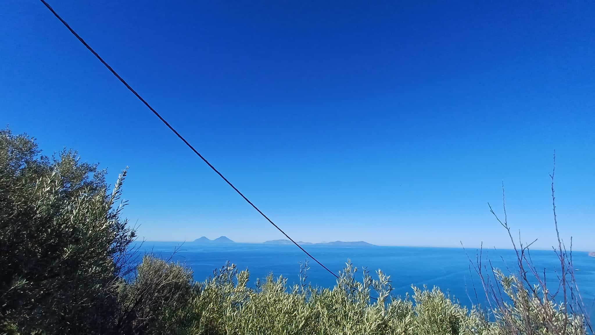 Vista panoramica del mare e delle isole dal punto di osservazione naturale, con vegetazione mediterranea in primo piano e cielo sereno.