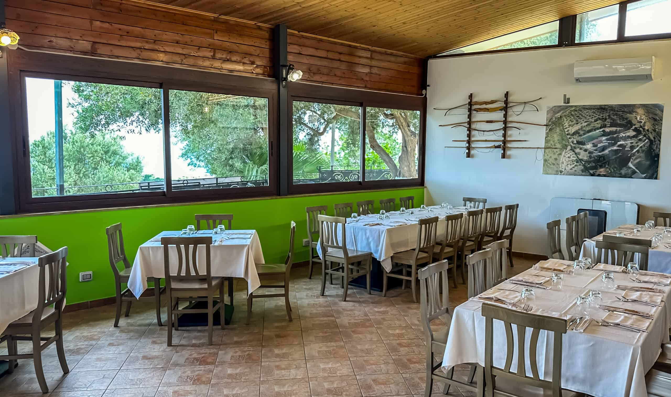 Tavolozza di un ristorante con grandi finestre che offrono una vista sulla natura, arredamento elegante con tavoli pronti per i clienti, atmosfera accogliente e luminosa, ideale per cene e pranzi conv.