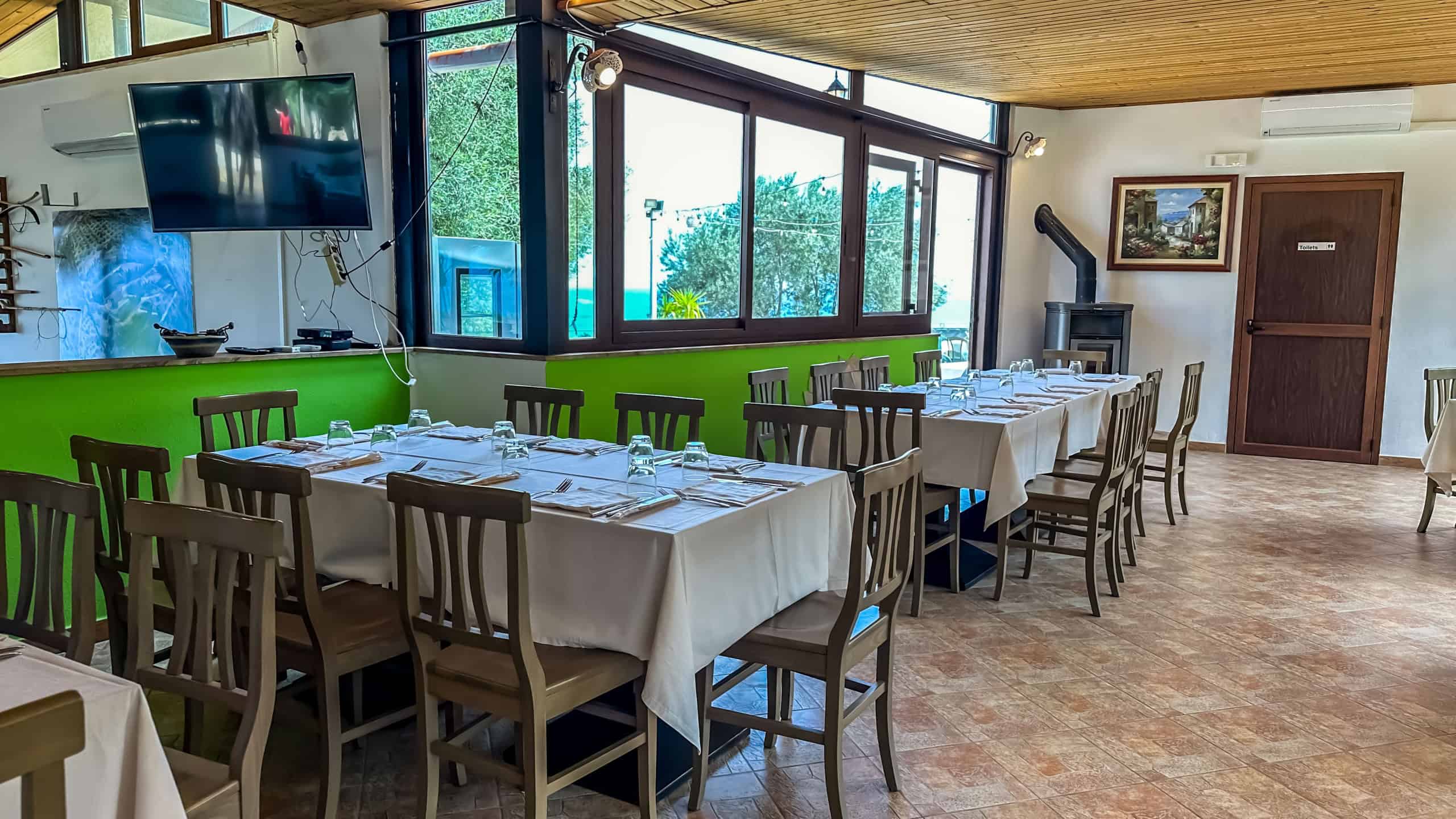 Tavolo da pranzo elegante in ristorante con sedie in legno, tovaglie bianche e ambiente accogliente con grandi finestre e vista naturale. Perfetto per cene conviviali e incontri di gruppo.