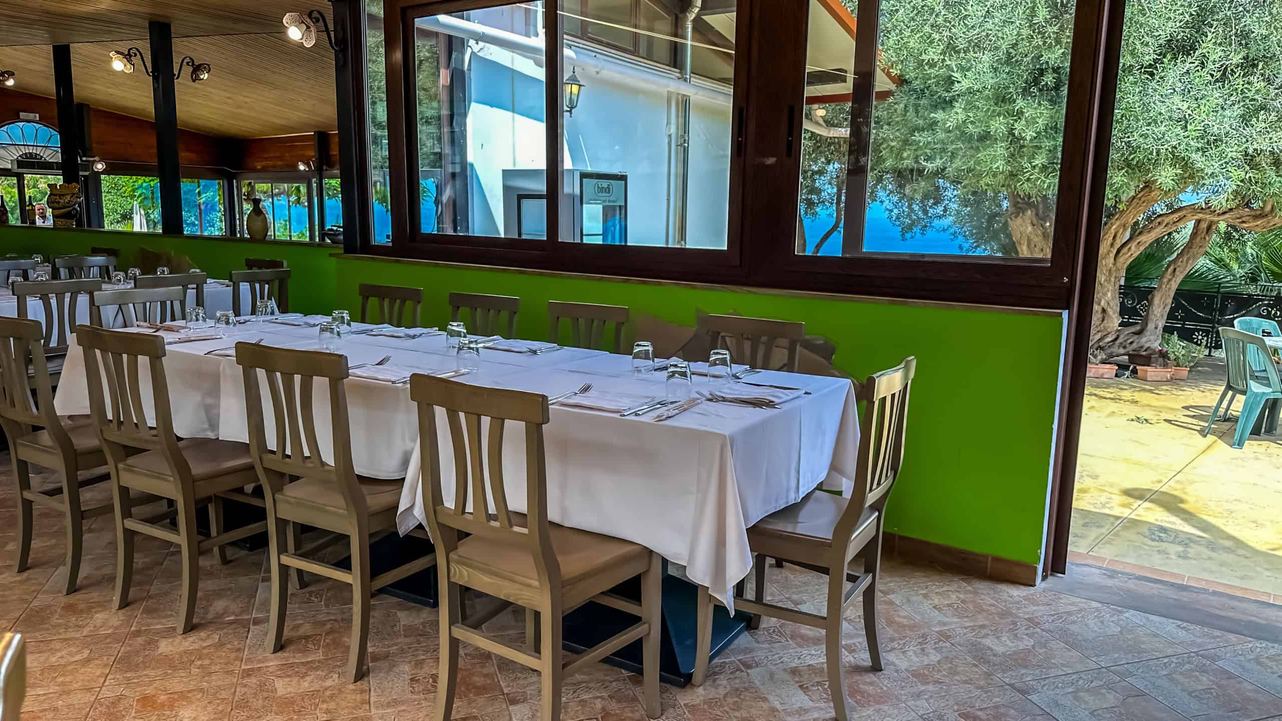 Tavolo da pranzo elegante in ristorante con grandi finestre che offrono vista sul giardino esterno, arredamento moderno e atmosfera accogliente, ideale per cene conviviali.