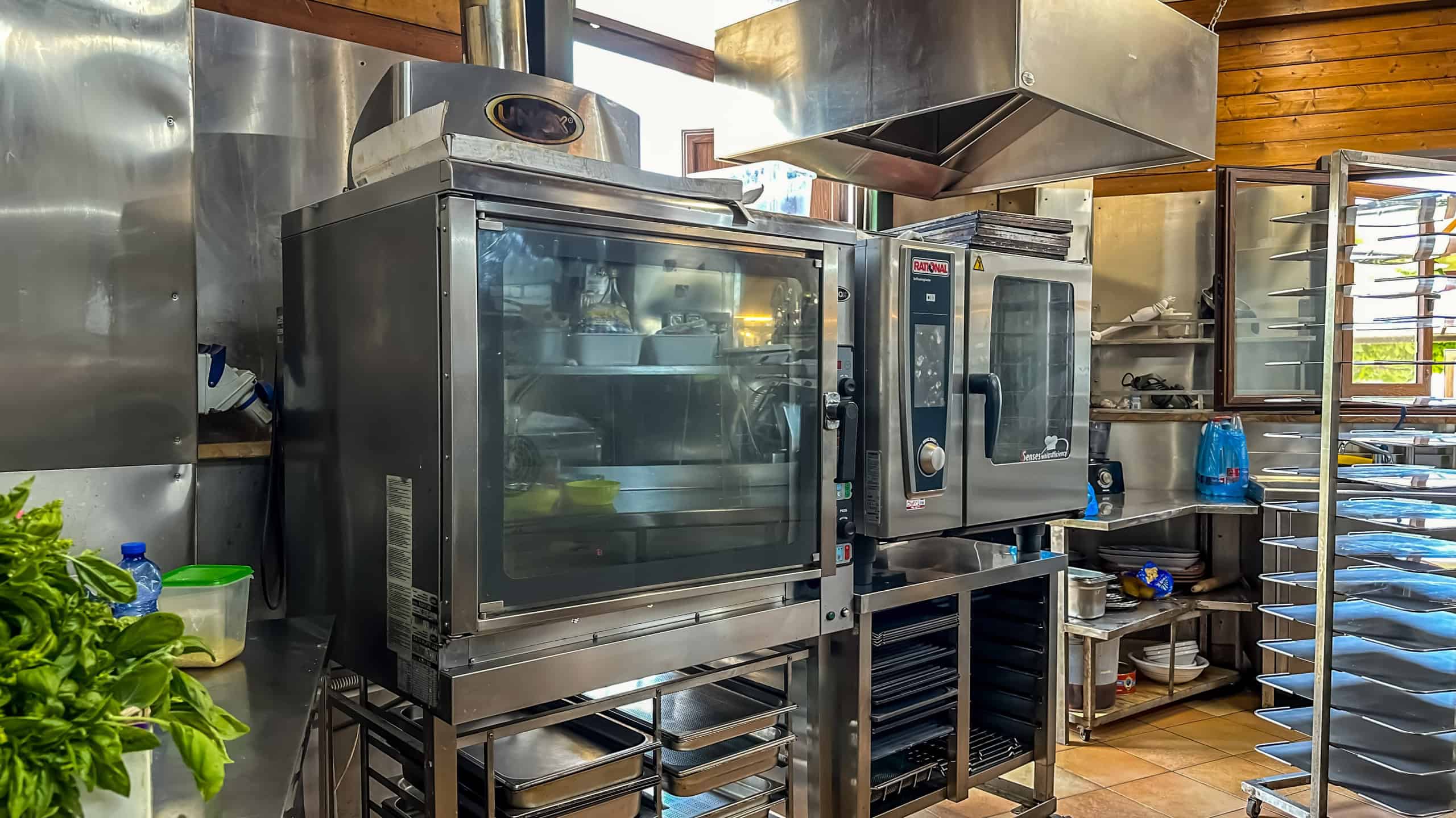 Aggiunta di un forno professionale in una cucina commerciale con attrezzature in acciaio inox e scaffalature per la preparazione di cibi di alta qualità.