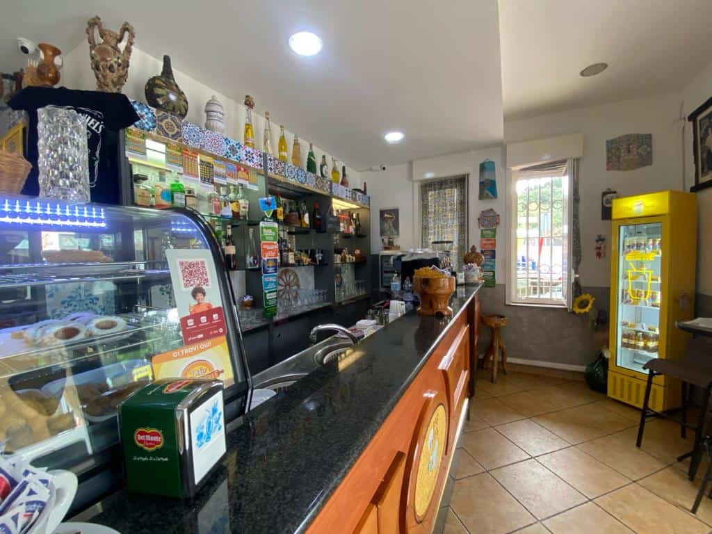 Un'area di caffetteria accogliente con bancone in legno, esposizione di dolci e bevande, decorazioni colorate e un ambiente luminoso ideale per gustare un caffè o uno spuntino.