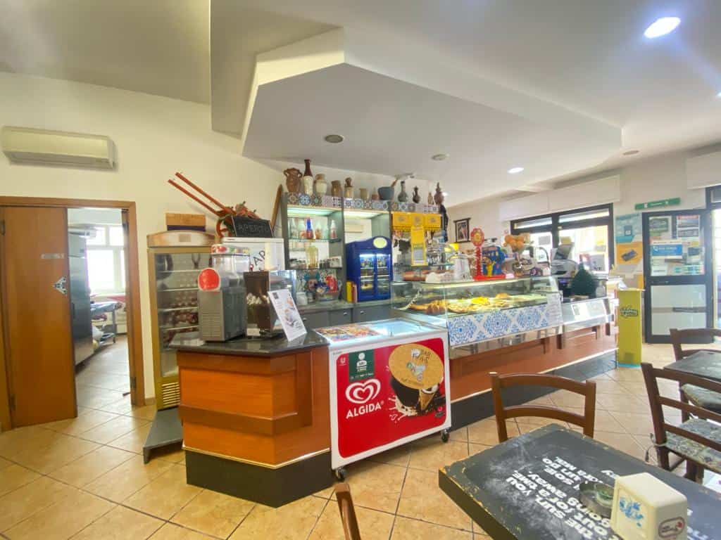 Mensa di un bar o caffetteria con esposizione di dolci e bevande, arredamento accogliente e atmosfera invitante, ideale per gustare snack e bevande in un ambiente rilassante.