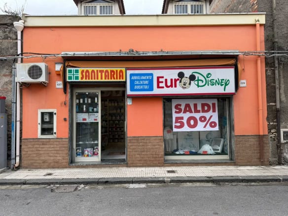 Pompa di calore installata su un negozio di articoli sanitari e giocattoli con segnale di saldi del 50%, edificio con pareti arancioni e dettagli in pietra, vetrina con prodotti in esposizione, in un.