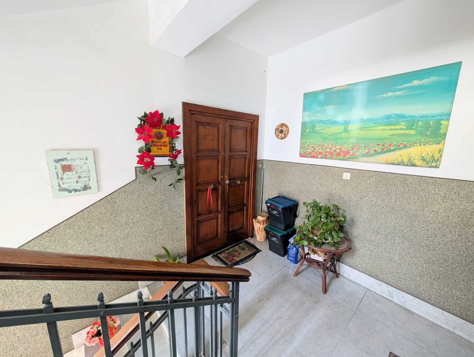 Entrata di un appartamento con porta in legno, decorazioni floreali e quadri artistici, in un ambiente luminoso e accogliente, ideale per servizi di intermediazione immobiliare NextCasa.