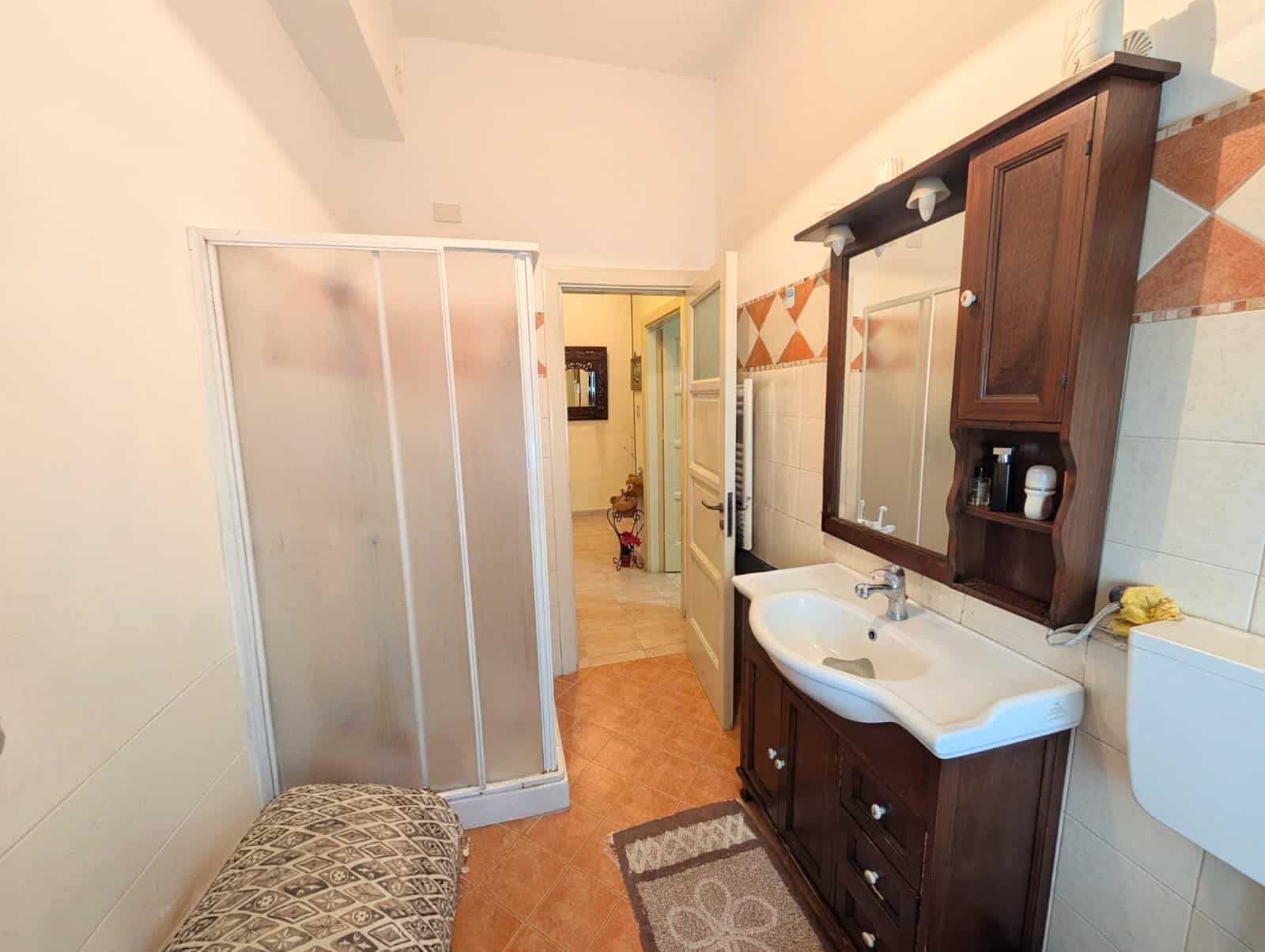 Pannello doccia in vetro trasparente, lavabo in ceramica con mobile in legno scuro, bagno spazioso e luminoso con pareti decorate, accessori da bagno e specchio grande, ambiente funzionale e accoglien.